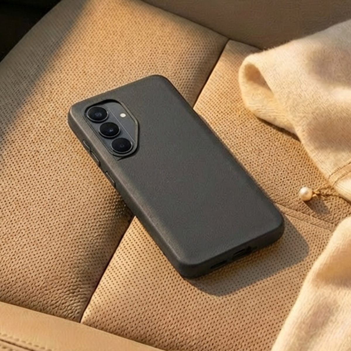 Ein schwarzes Smartphone mit drei Kameras liegt auf einem braunen, perforierten Sitz.