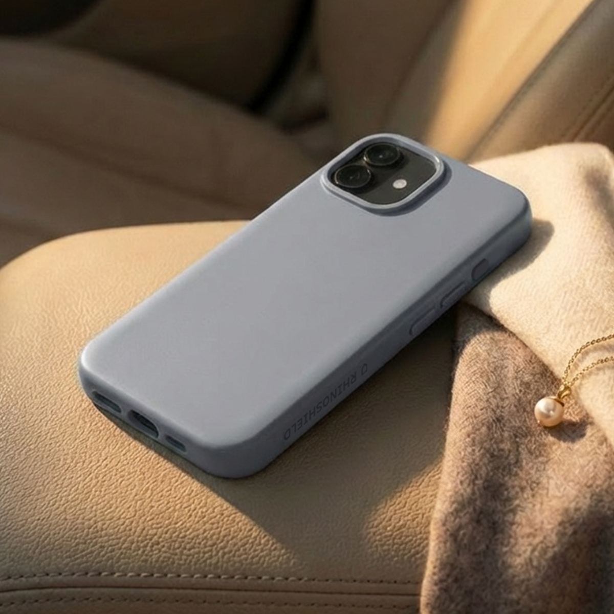 Una custodia grigia per telefono con rigonfiamento della fotocamera poggia su tessuto beige accanto a una collana di perle.