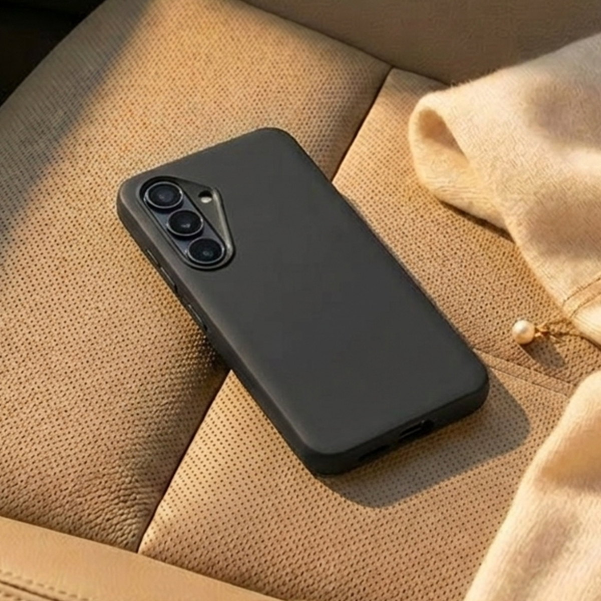 Una custodia nera per telefono con tre fotocamere giace su una superficie'tan'testurizzata.
