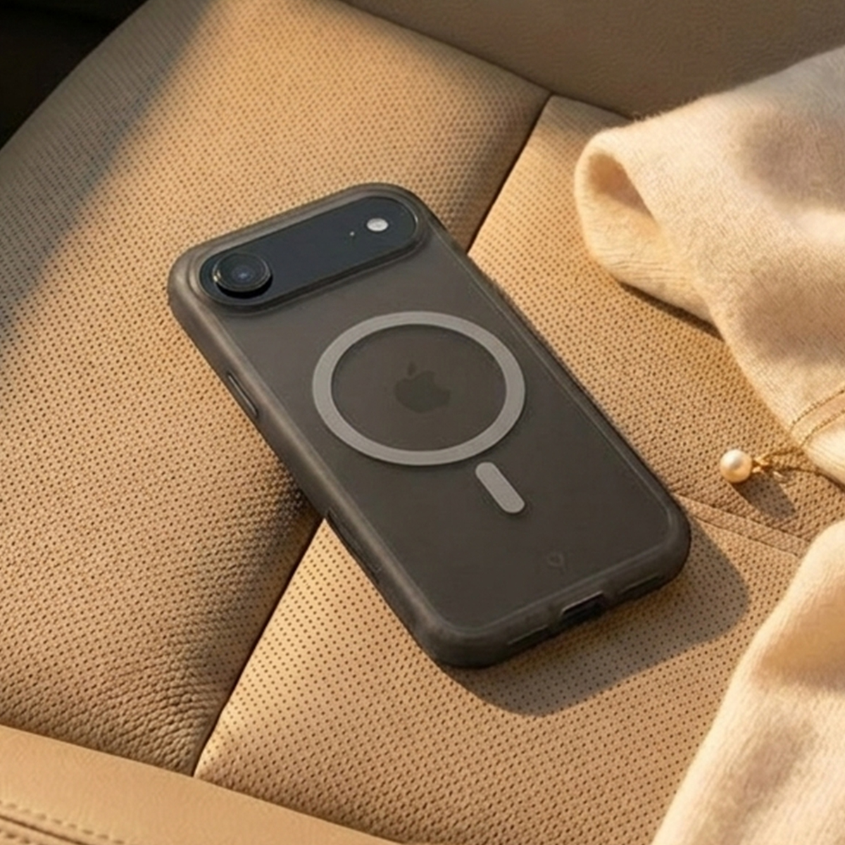 Ein schwarzes iPhone mit MagSafe-Hülle liegt auf beigefarbenem Autositz.