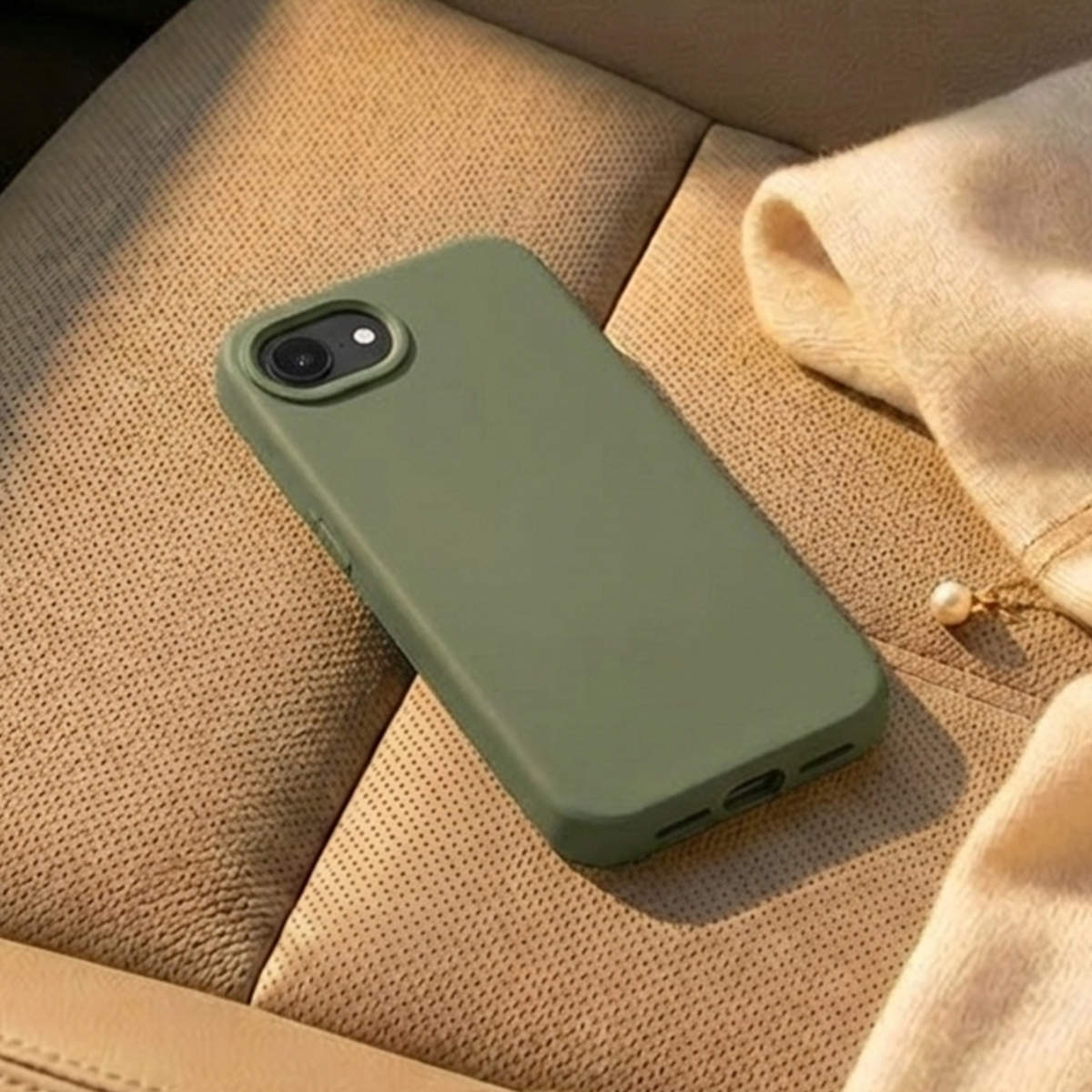 Ein grünes Handy mit Hülle liegt auf einem beigefarbenen Autositz neben einem Pullover.