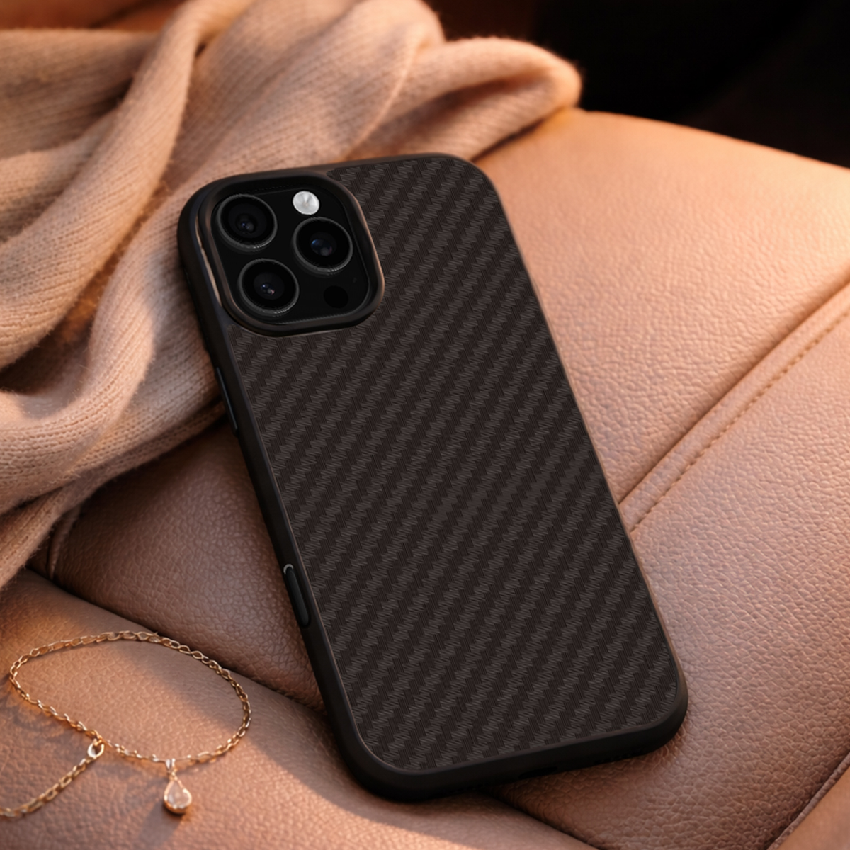 Un iPhone nero con motivo in fibra di carbonio poggia sulla pelle, con una collana d'oro nelle vicinanze.