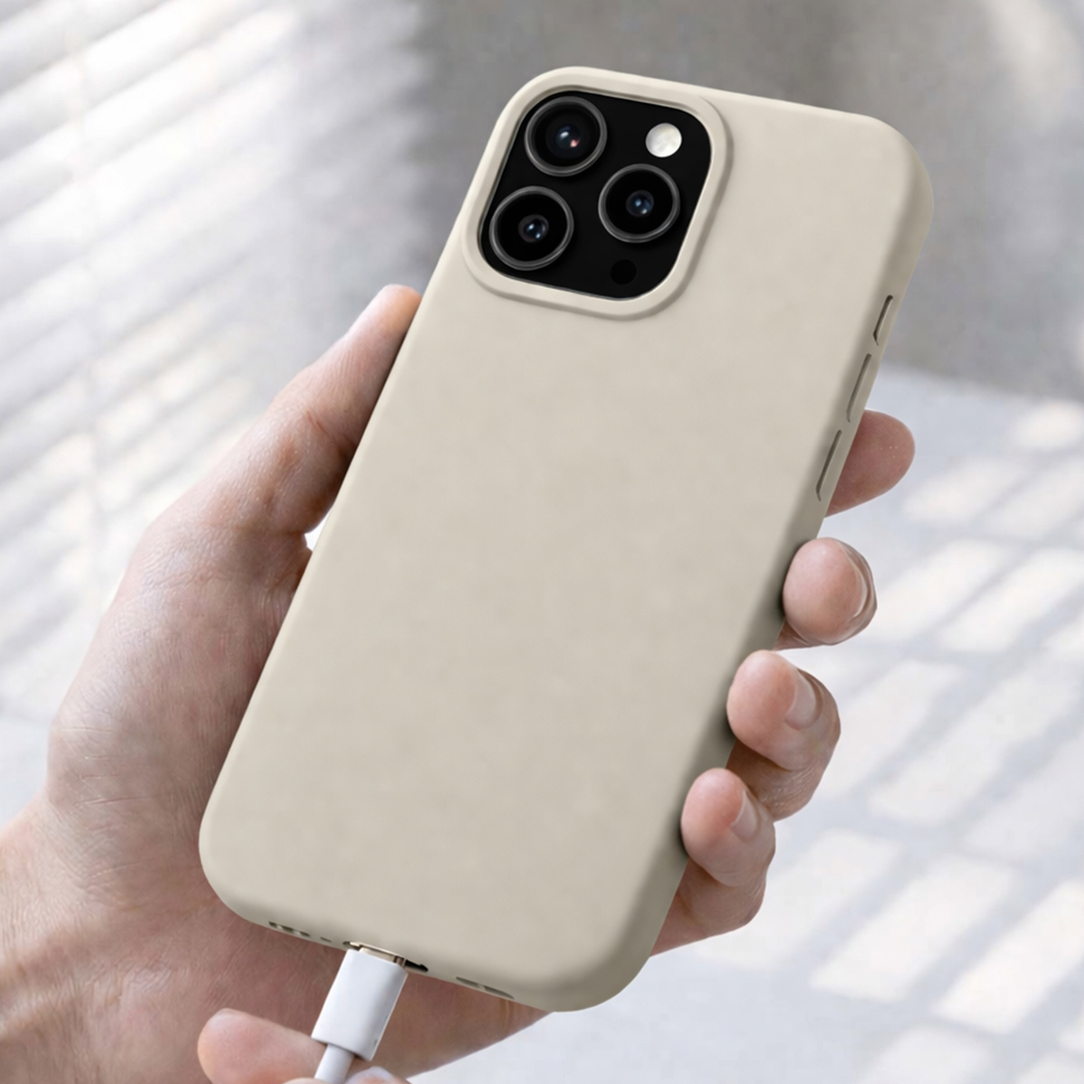 Una mano tiene una custodia beige per iPhone con un cavo di ricarica collegato.