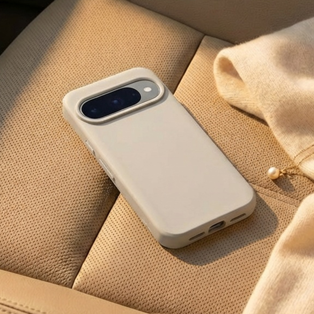 Un telefono grigio chiaro con fotocamere su un sedile in pelle beige.