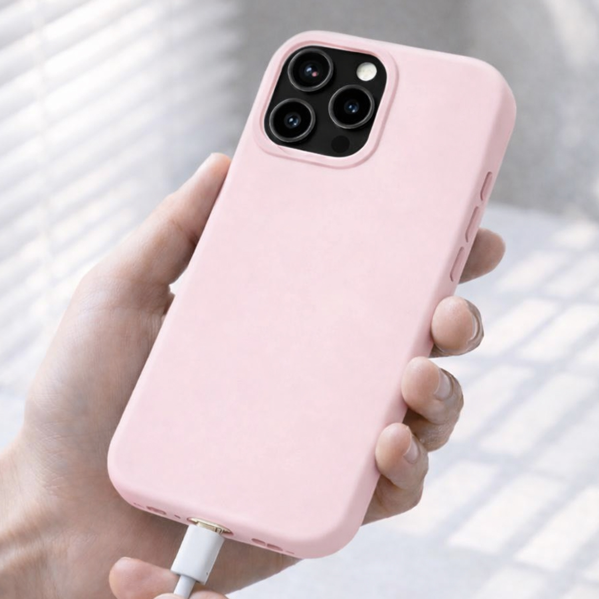 Una mano tiene un telefono rosa con tre fotocamere e un cavo di ricarica collegato.