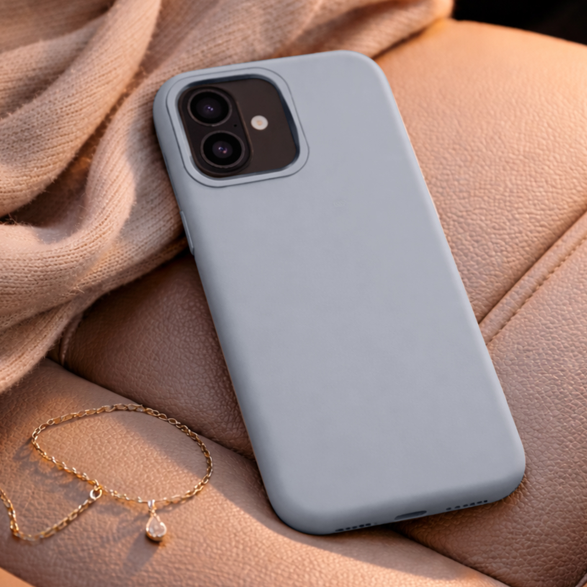 Telefono grigio su pelle e tessuto, accanto a una collana d'oro con ciondolo.