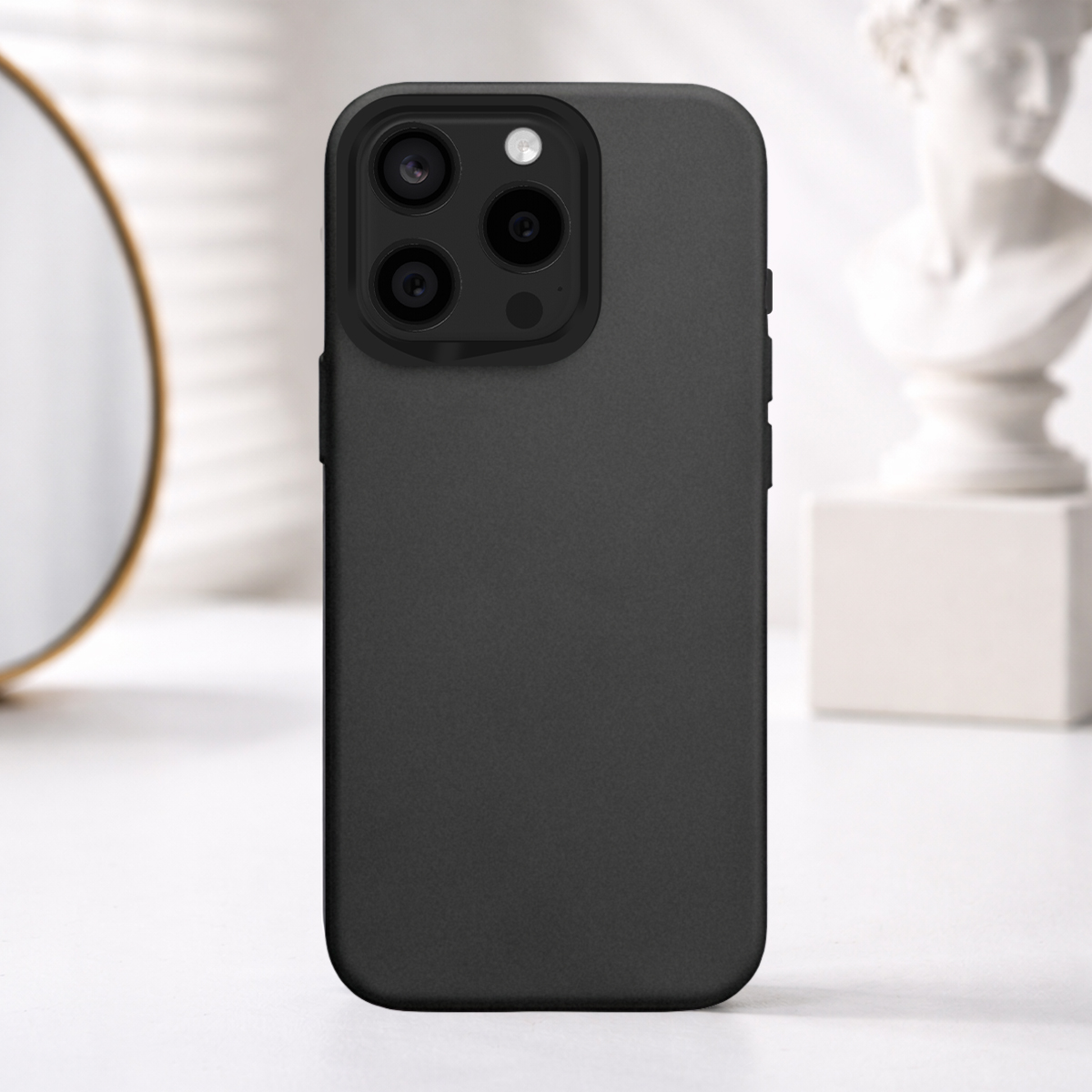 Coque de téléphone noire avec triple appareil photo, sur une table avec miroir et sculpture.