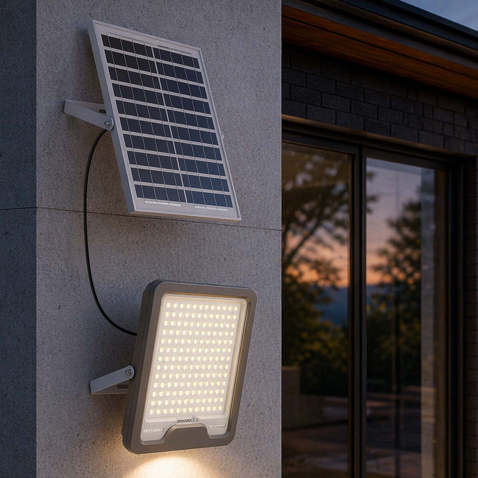 Ein Solarpanel und ein LED-Strahler sind an einer Wand montiert. Draußen Dämmerung.