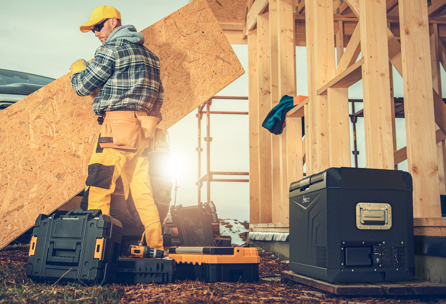 Operaio porta pannello legno, cassette attrezzi e frigo in cantiere.