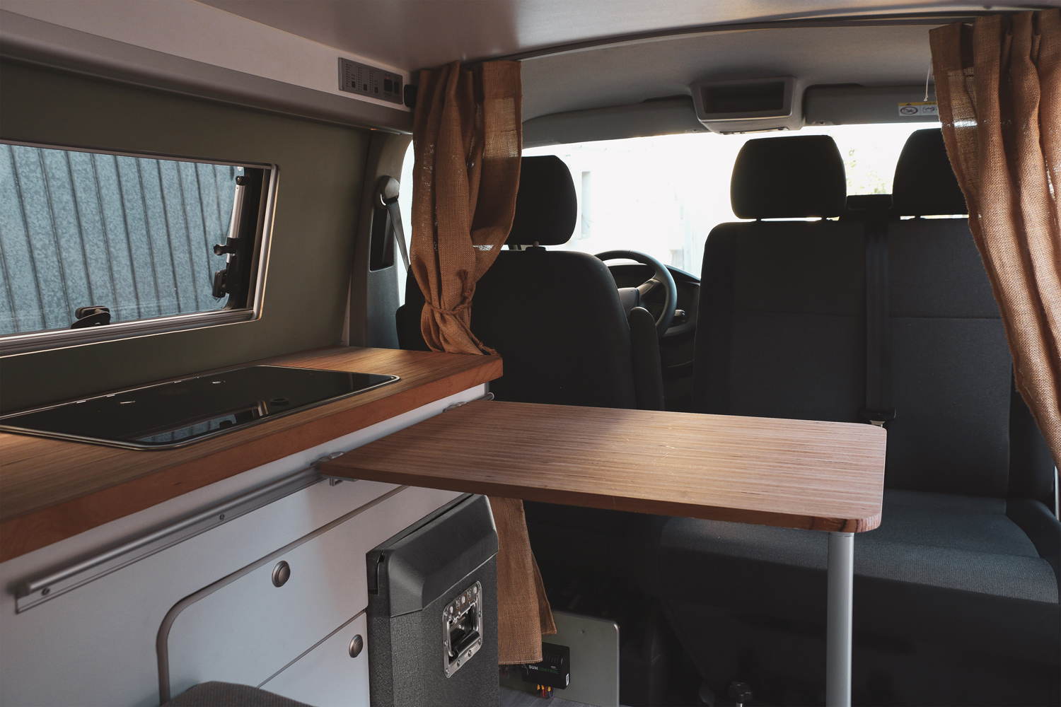 Wnętrze kampera z aneksem kuchennym, rozkładanym stołem i siedzeniami.