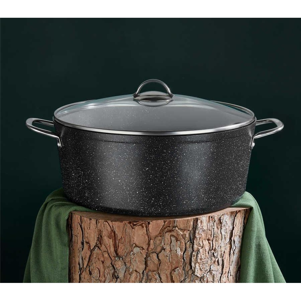 Yeşil kumaşlı kütük üzerinde cam kapaklı siyah tencere.