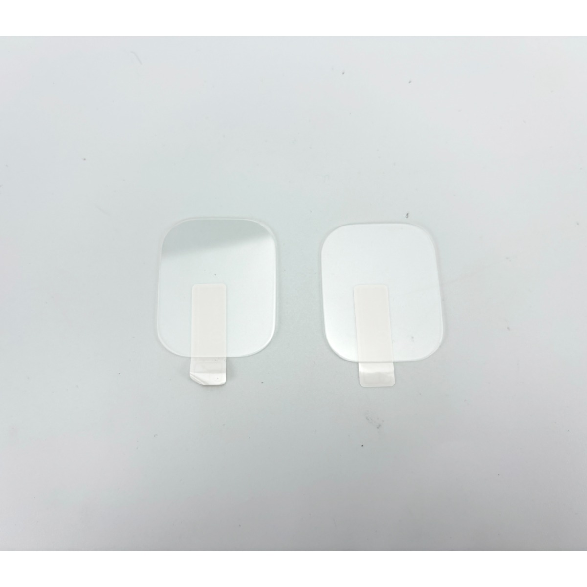 Due pellicole protettive trasparenti per schermo con nastro bianco su sfondo grigio.
