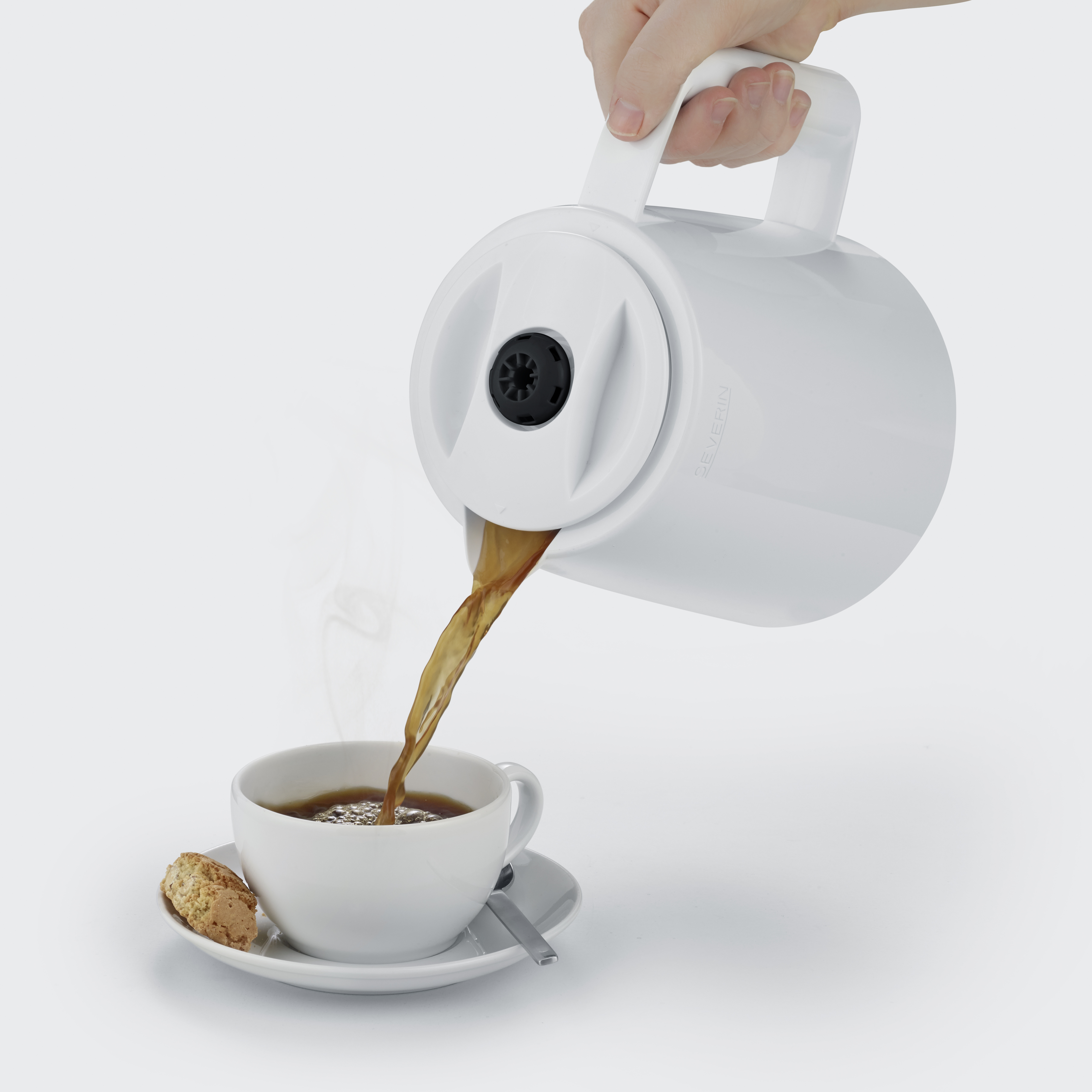 Una mano versa caffè da una brocca bianca in una tazza con un biscotto.