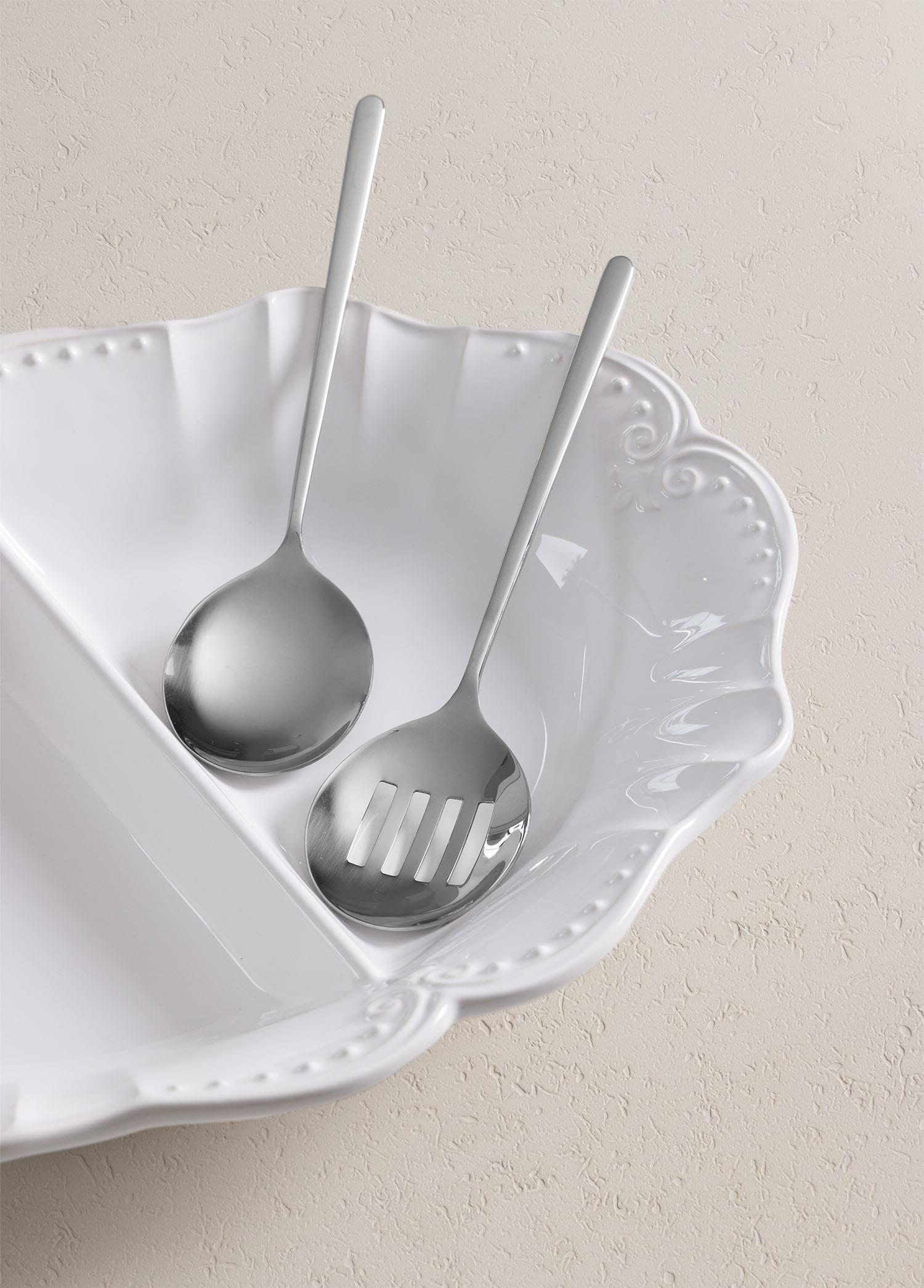 Dokuya sahip bir yüzey üzerinde beyaz seramik kapta iki metal servis kaşığı.