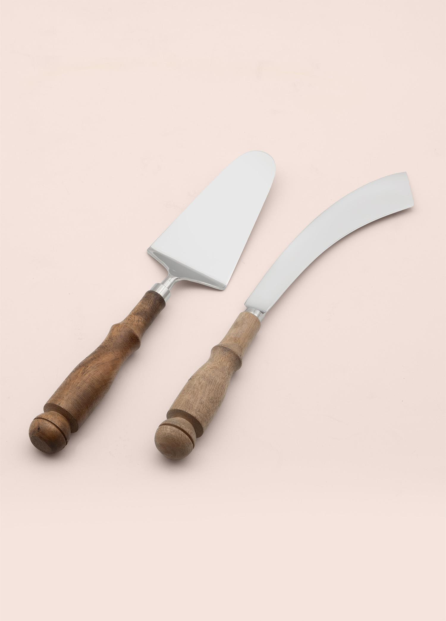 Ahşap saplı bir pasta servis spatulası ve eğri bıçak, pembe arka planda.