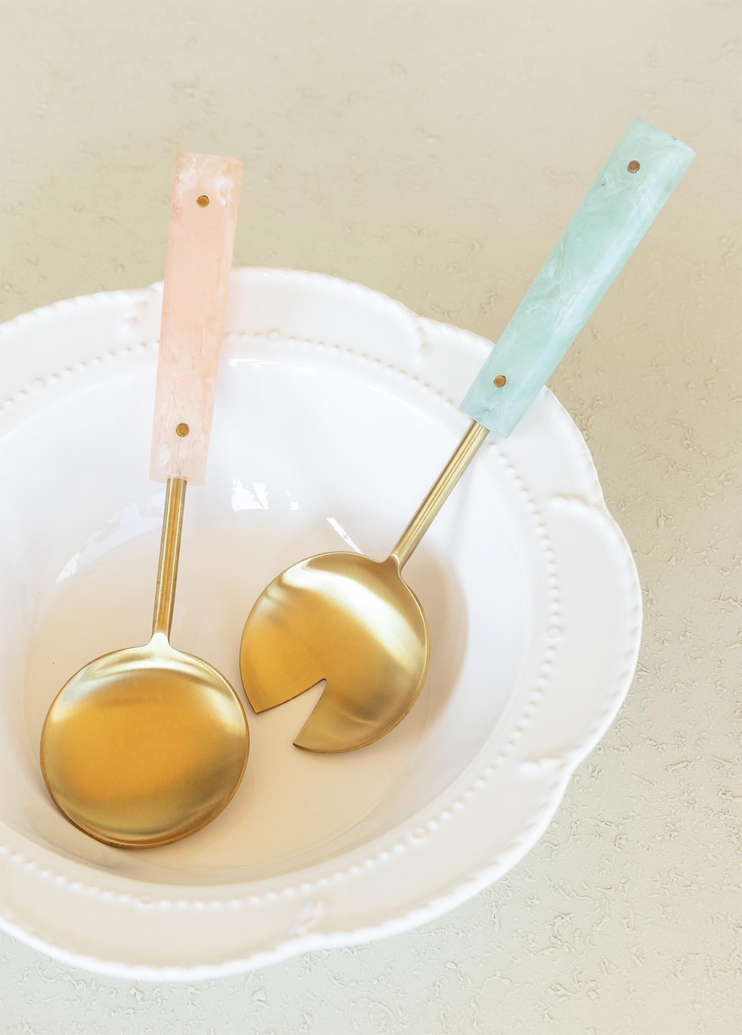 Beyaz bir kasede pastel saplı altın servis kaşıkları.