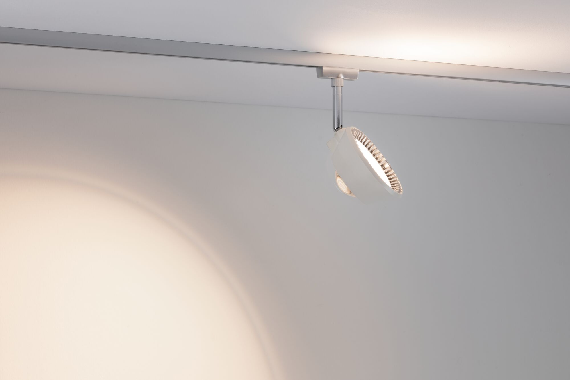 Ein weißer Schienenstrahler beleuchtet eine weiße Wand mit einem hellen Lichtkreis.