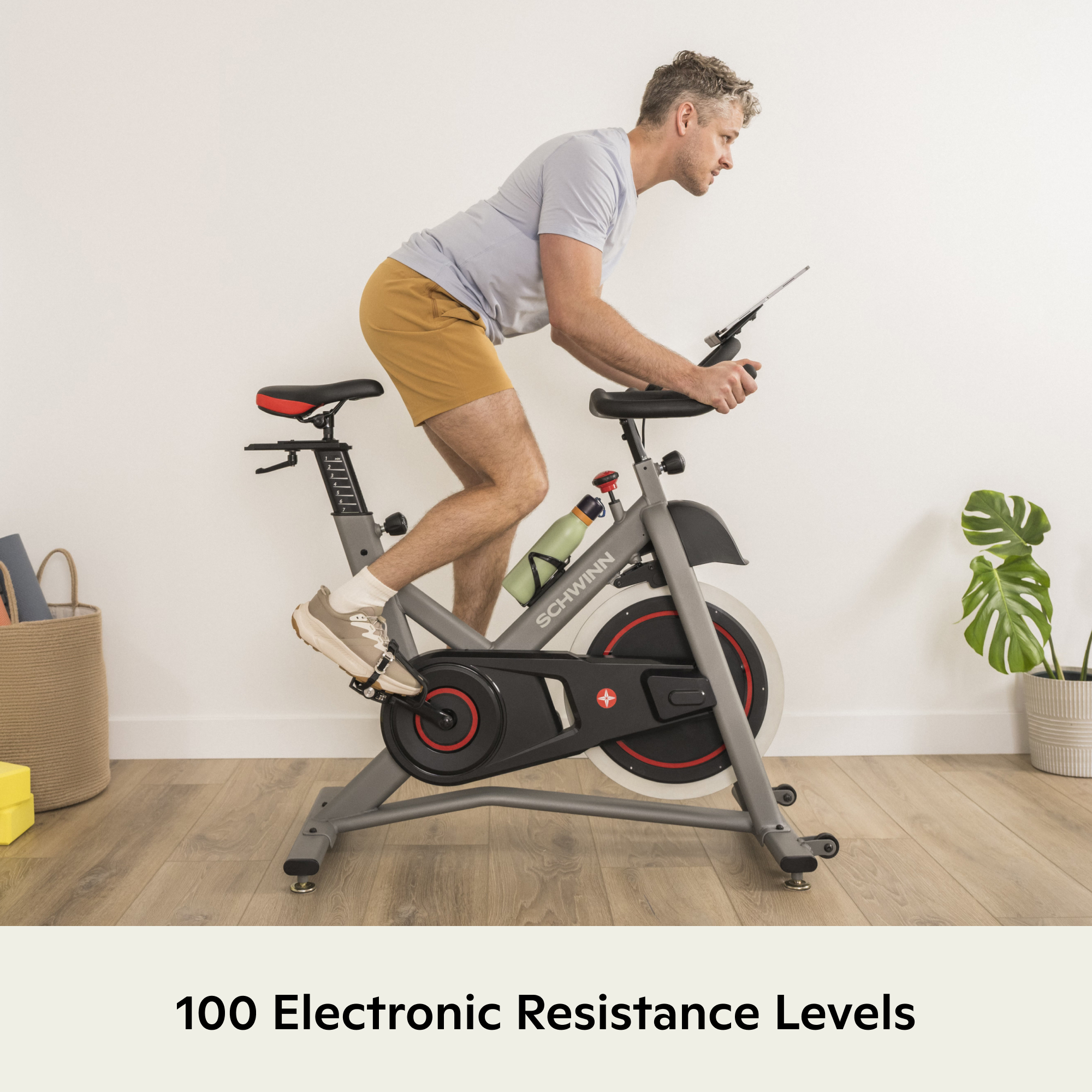 Homme sur vélo d'appartement avec tablette et bouteille d'eau. Intérieur avec plantes.