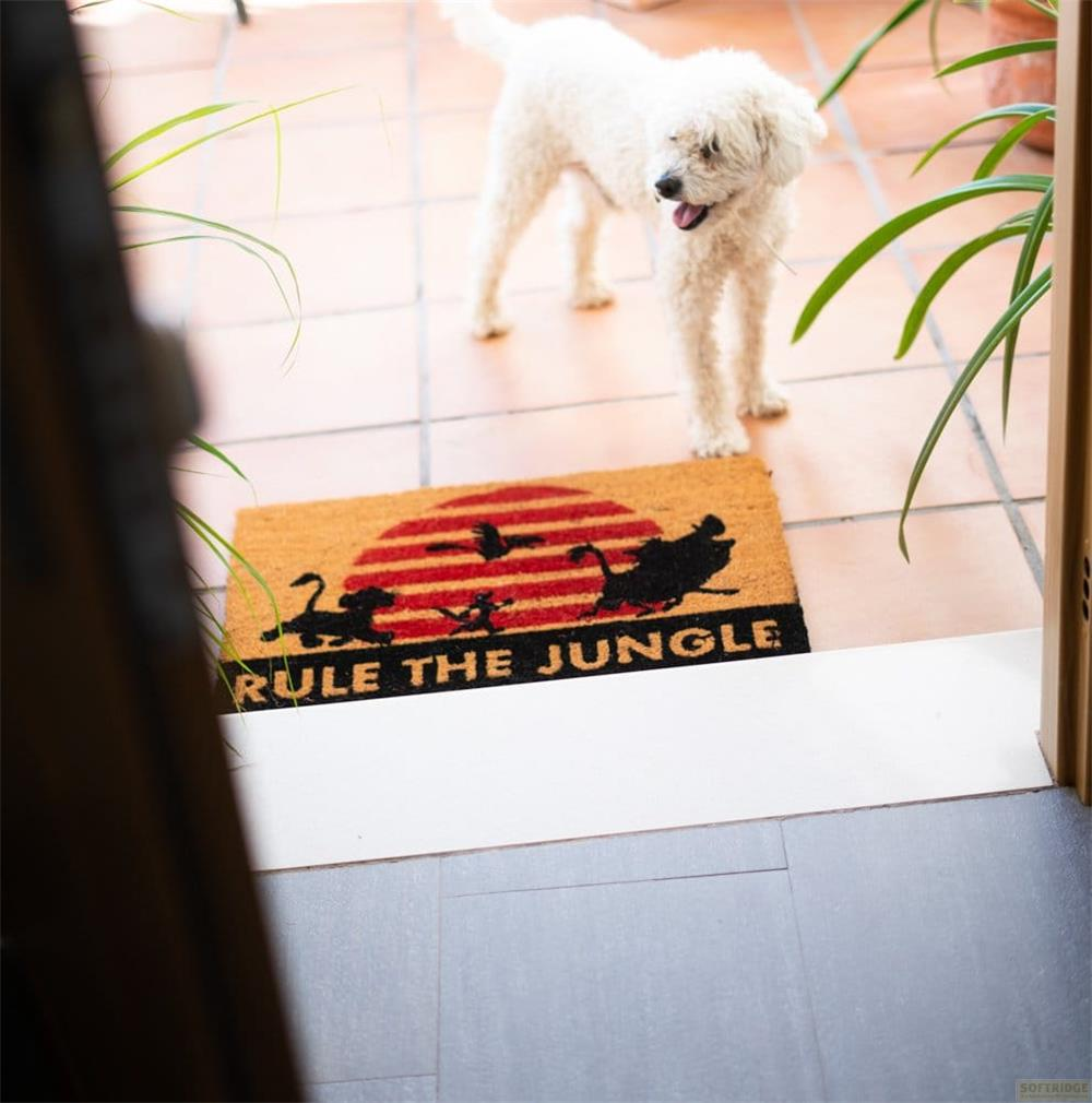 Un cane bianco è su piastrelle vicino a uno zerbino con scritto 'Rule the Jungle'.