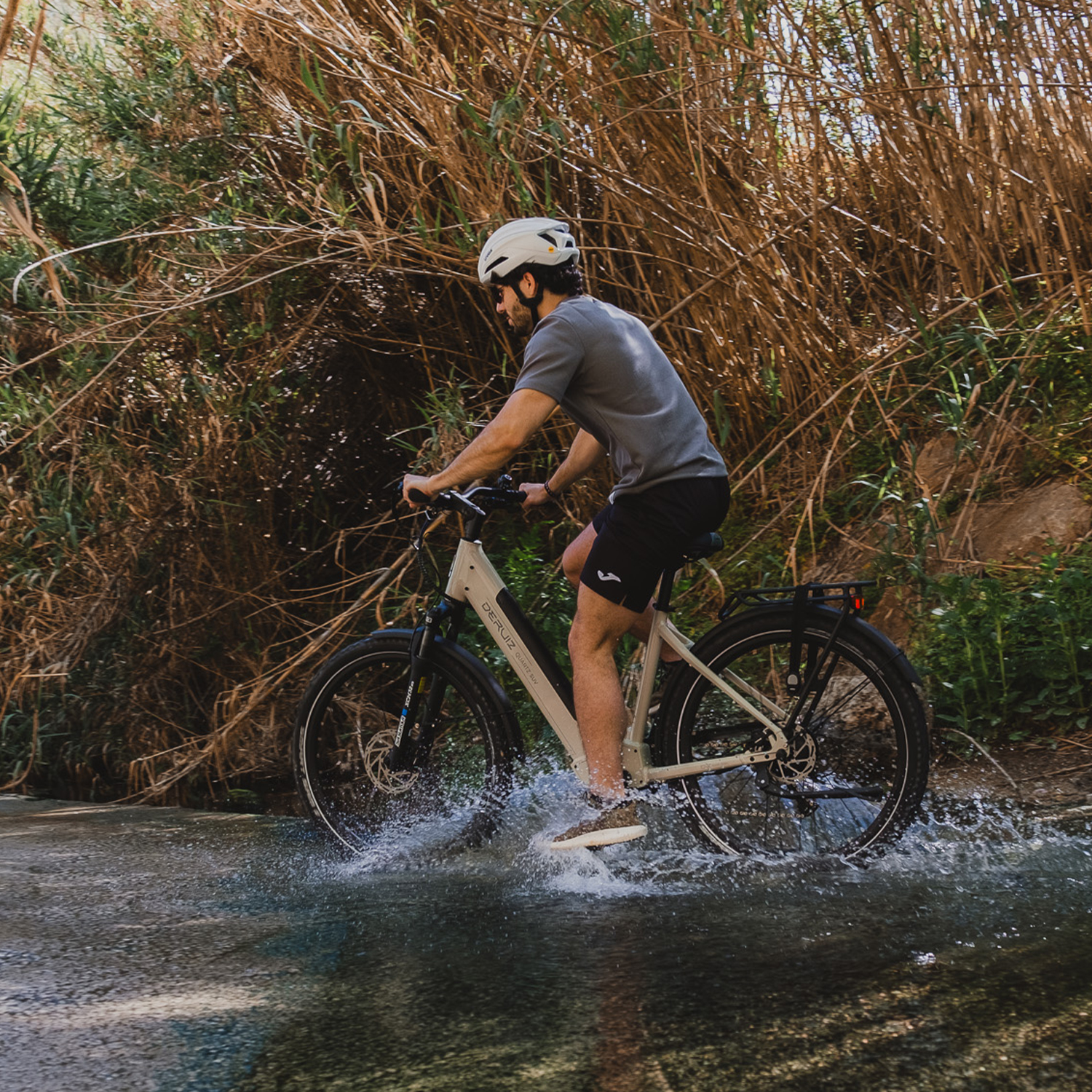 Mann fährt Fahrrad durch Wasser, umgeben von Vegetation.