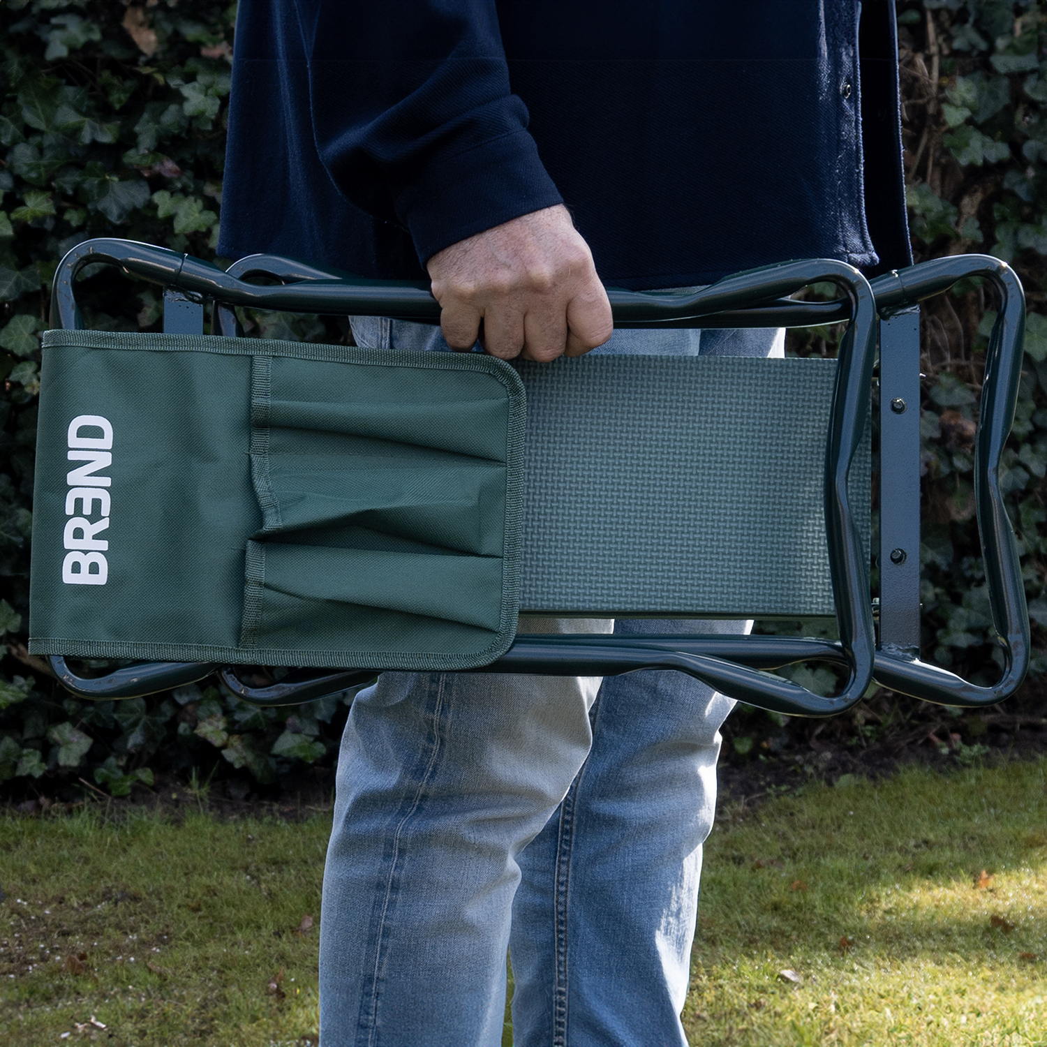 Un homme en jean porte un siège de jardin vert avec une pochette.