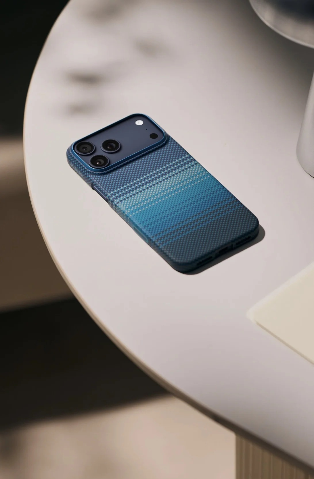 Un telefono blu con custodia a scacchi riposa su un tavolo bianco.