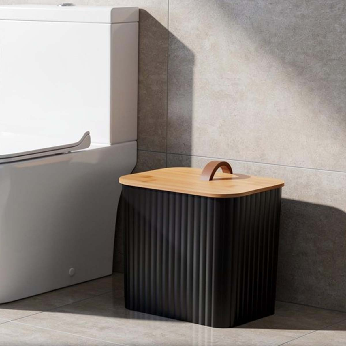 Ein schwarzer Behälter mit Holzdeckel neben einer weißen Toilette.