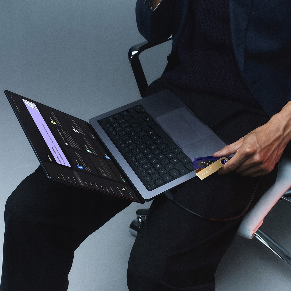 Osoba trzymająca złotą portmonetkę sprzętową podłączoną do laptopa. Ciemne tło.