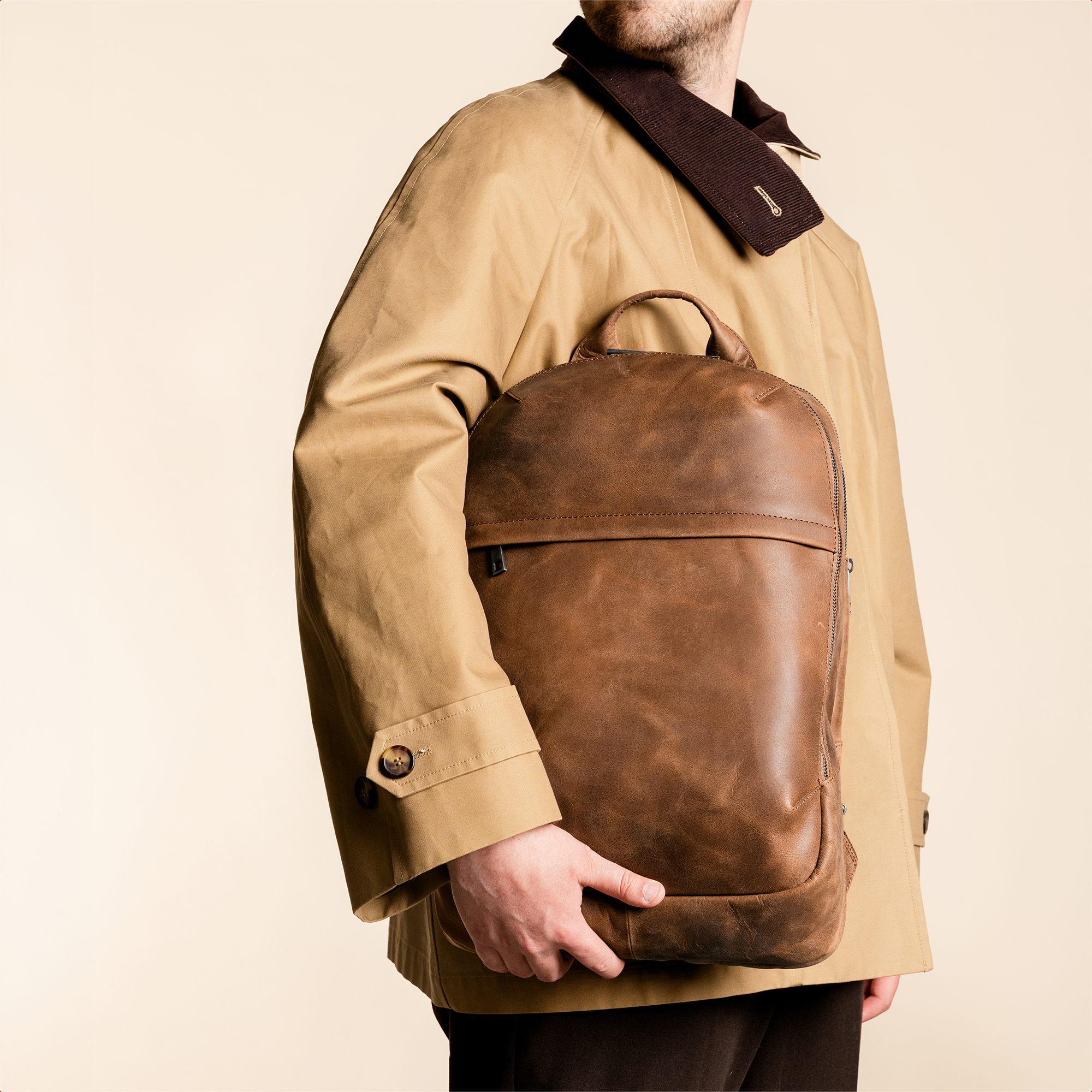 Man in beige jas met bruine leren rugzak