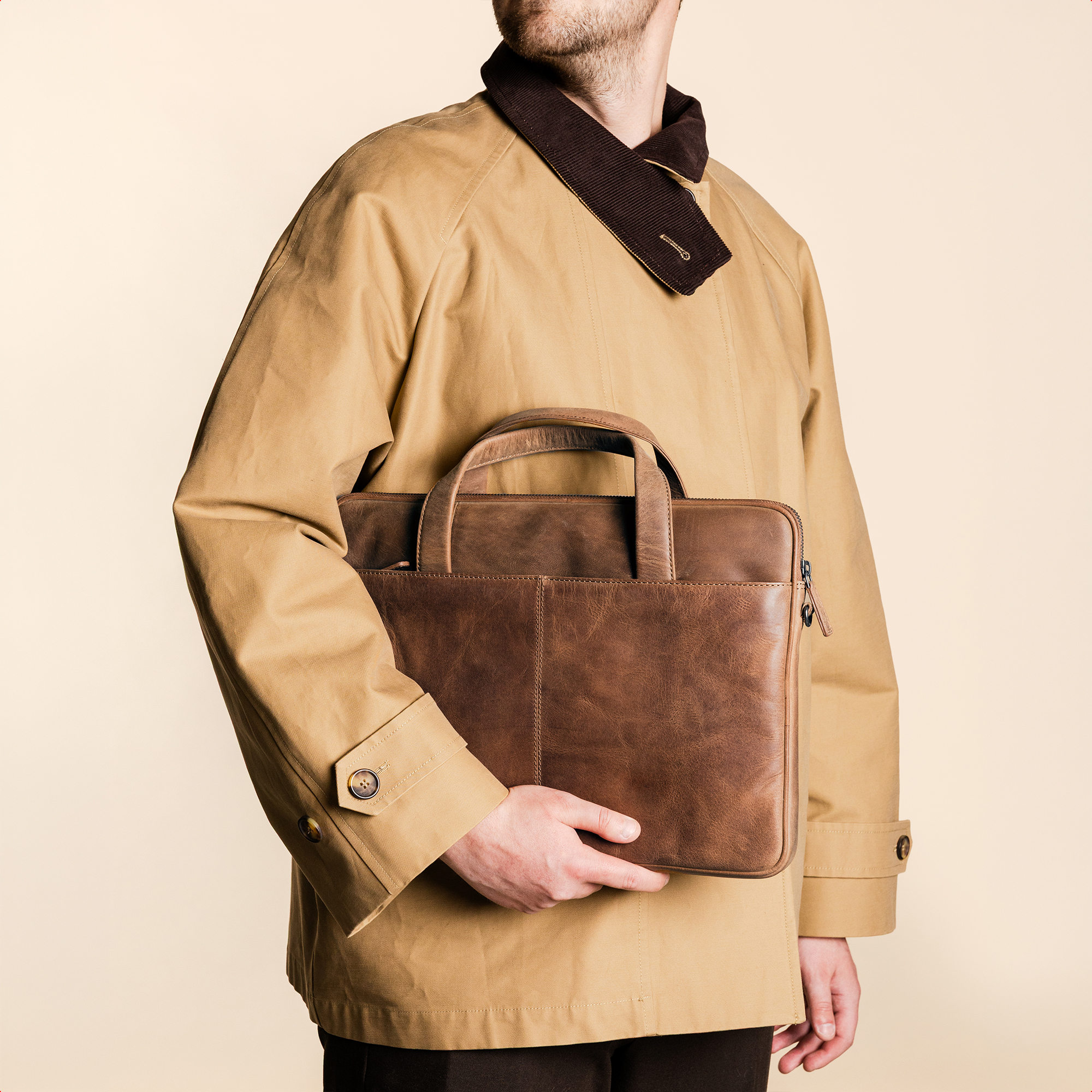 Man in beige jacket holds a brown leather briefcase.