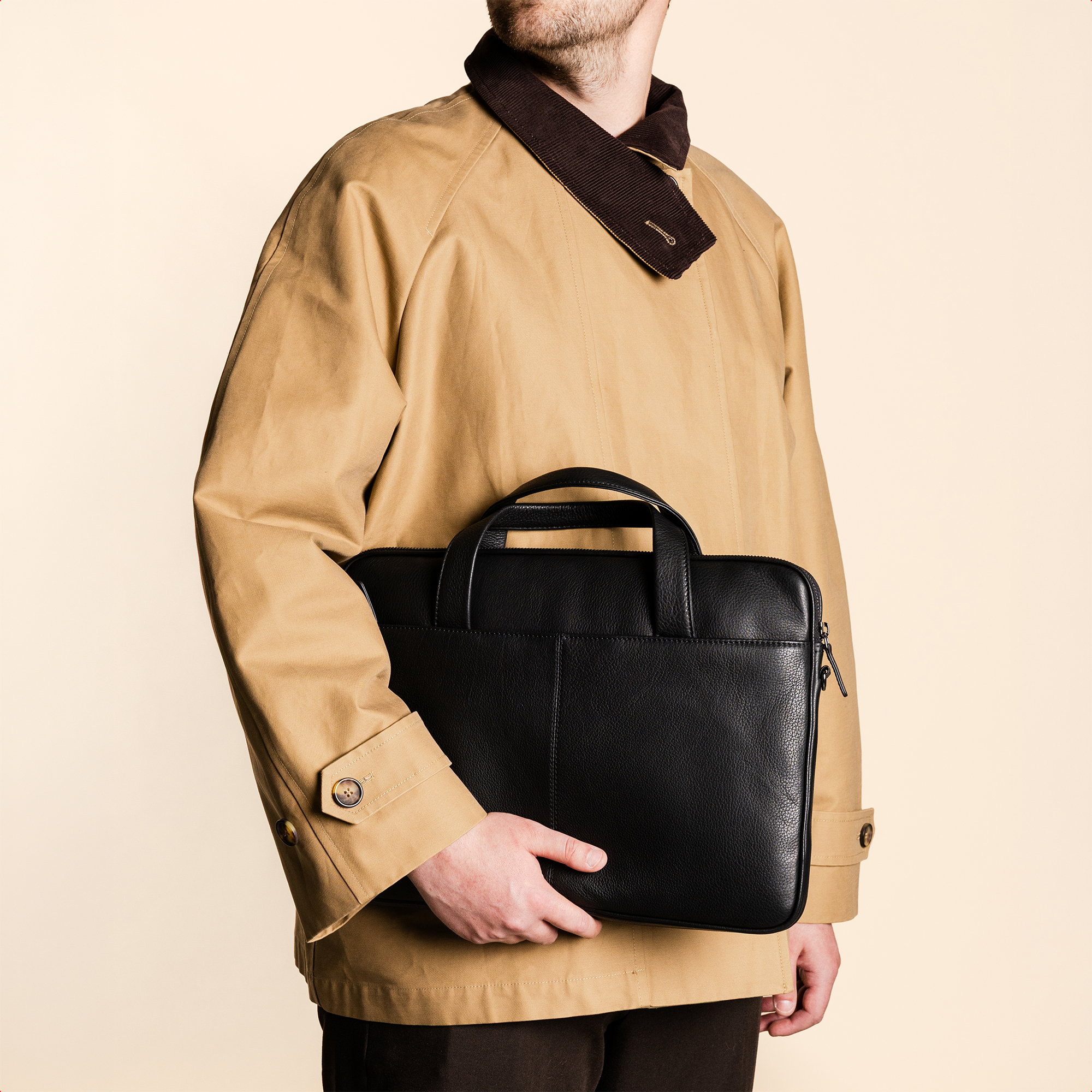 Man in tan coat holding a black laptop bag.