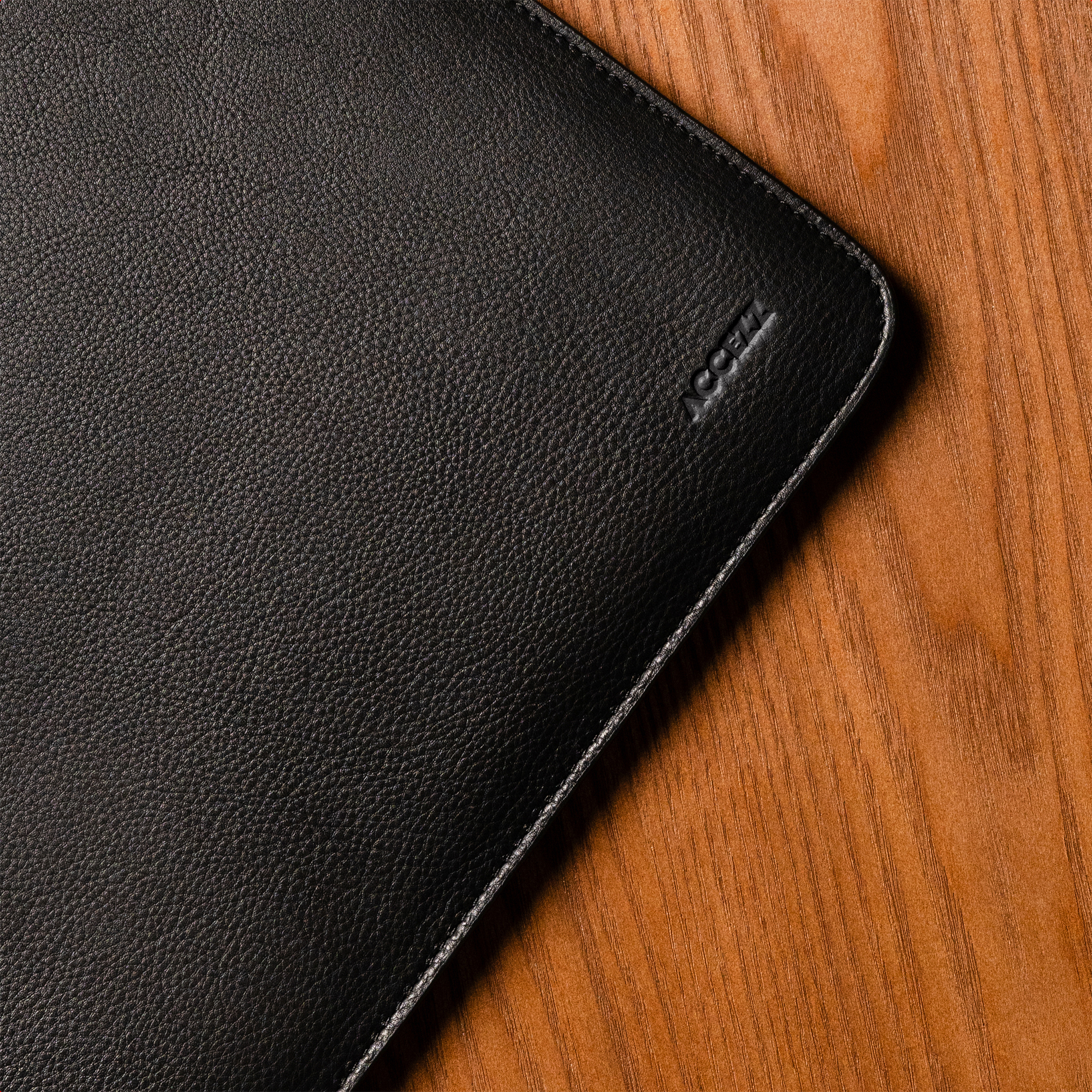Black leather product with embossed logo on a wooden surface.