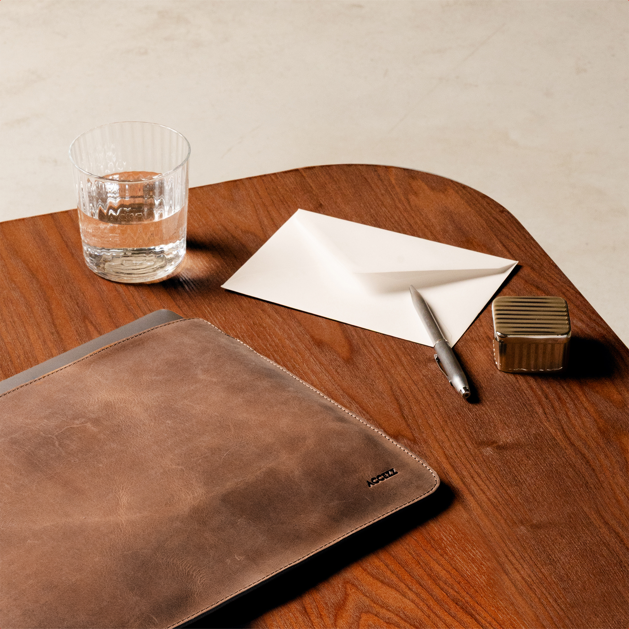 A glass of water, an envelope, a pen, and a gold box on a wooden table.