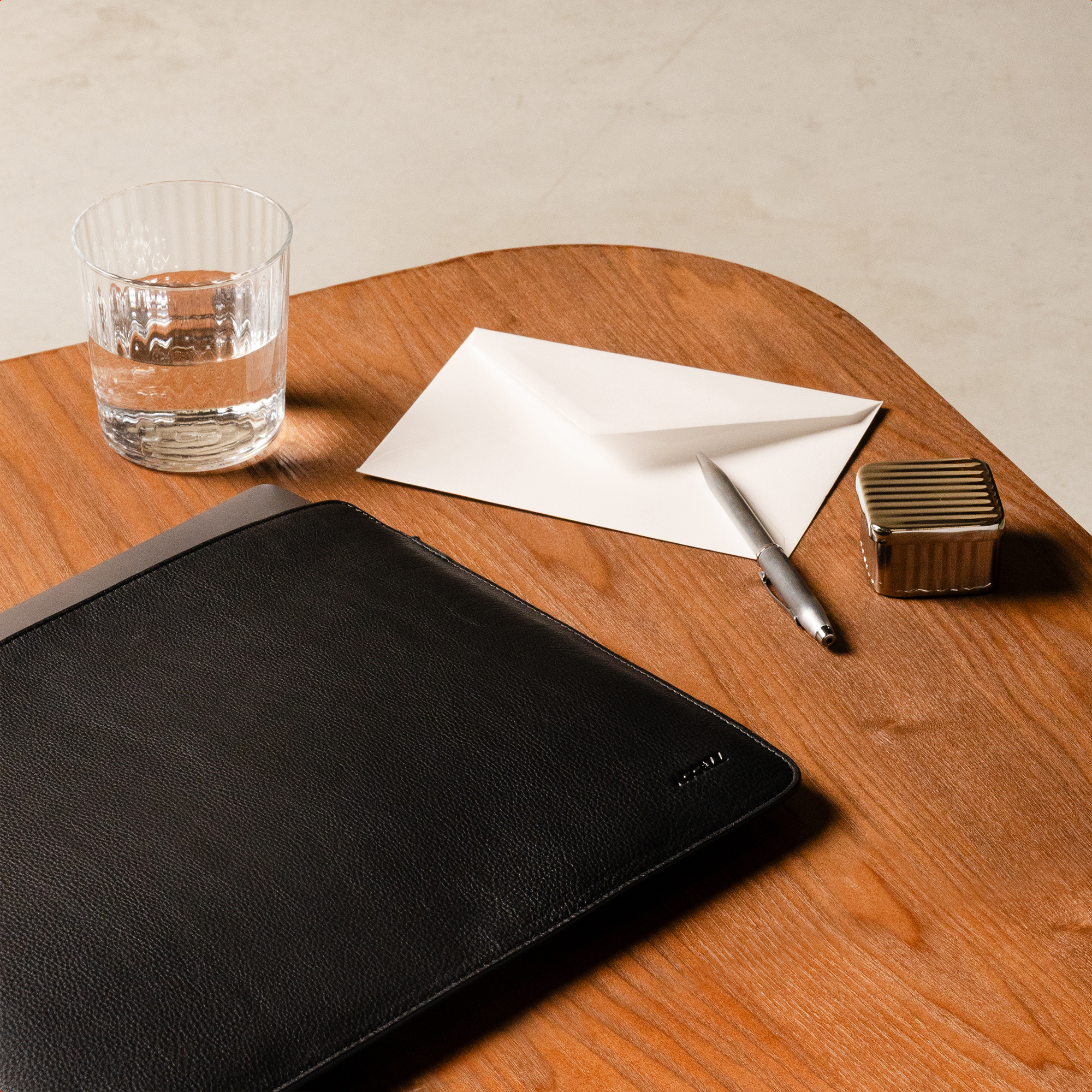A black leather folder, an envelope, pen, and glass of water on a wooden table.