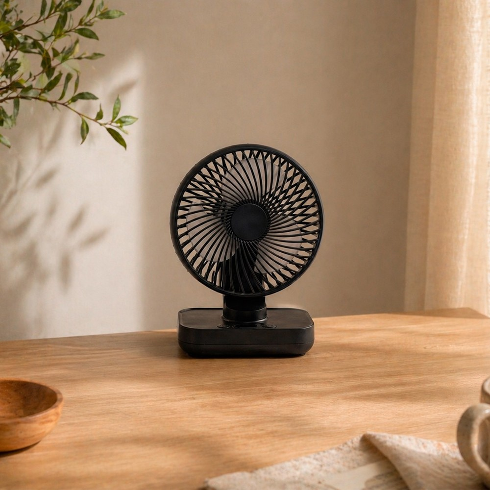 Un ventilador de mesa negro está sobre una mesa de madera junto a una planta.