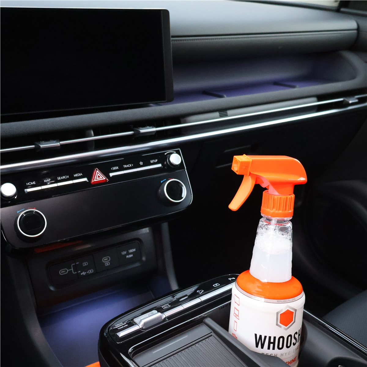 A spray bottle cleaner sits in a car's cup holder next to the dashboard.