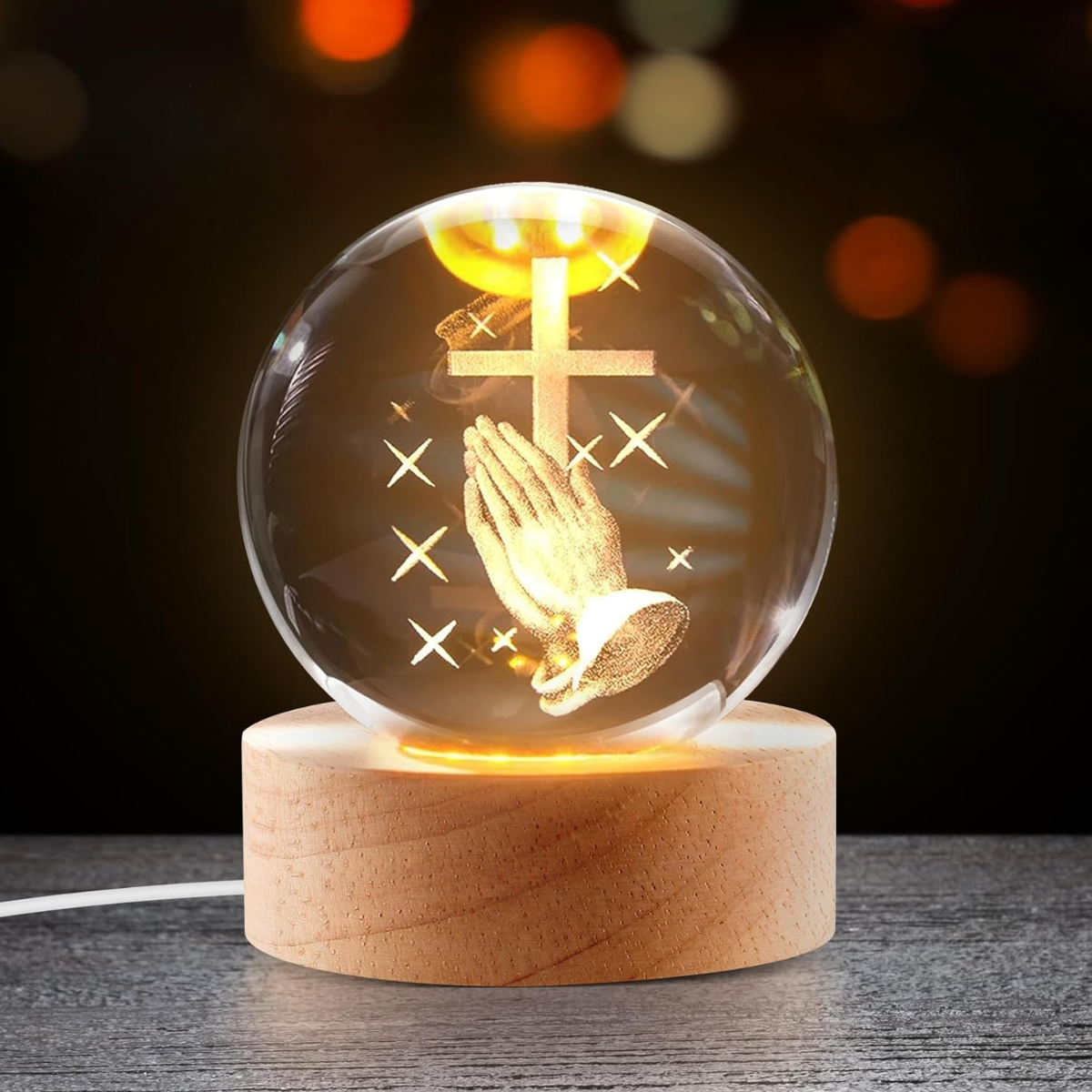 Kristallkugel mit betenden Händen und Kreuz, beleuchtet auf Holzsockel.