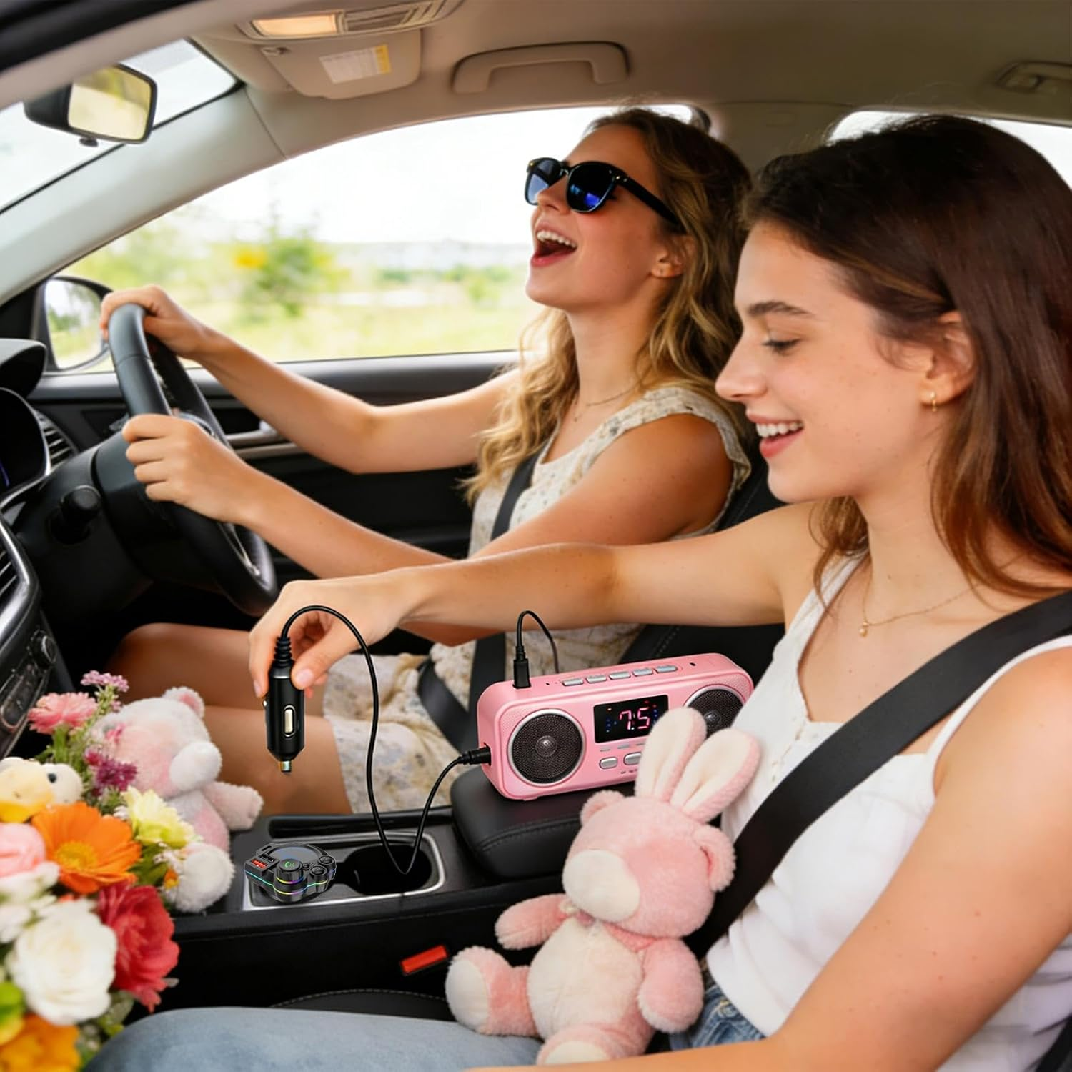 Zwei Mädchen fahren Auto, eine lachend, die andere singt. Rosa Radio, Stofftiere, Blumen.