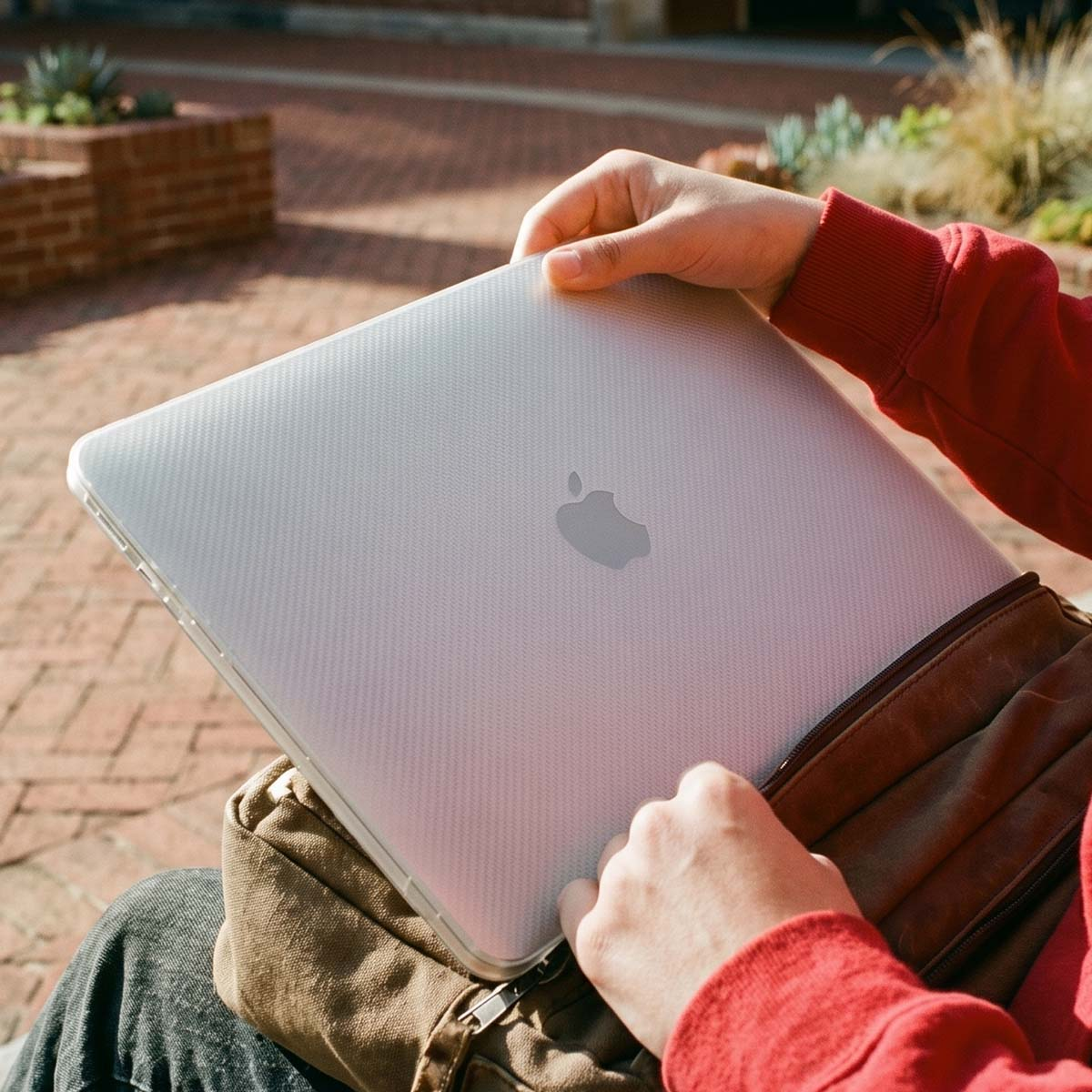 Person mit rotem Pullover legt ein MacBook in eine braune Tasche.