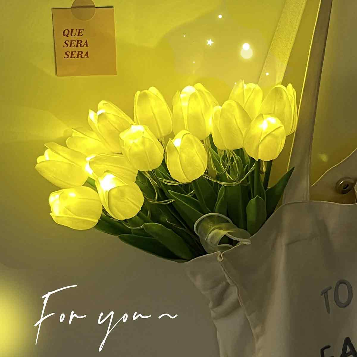 Gelbe Tulpen mit Lichterkette auf einer Tasche mit Notiz 'QUE SERA SERA'.