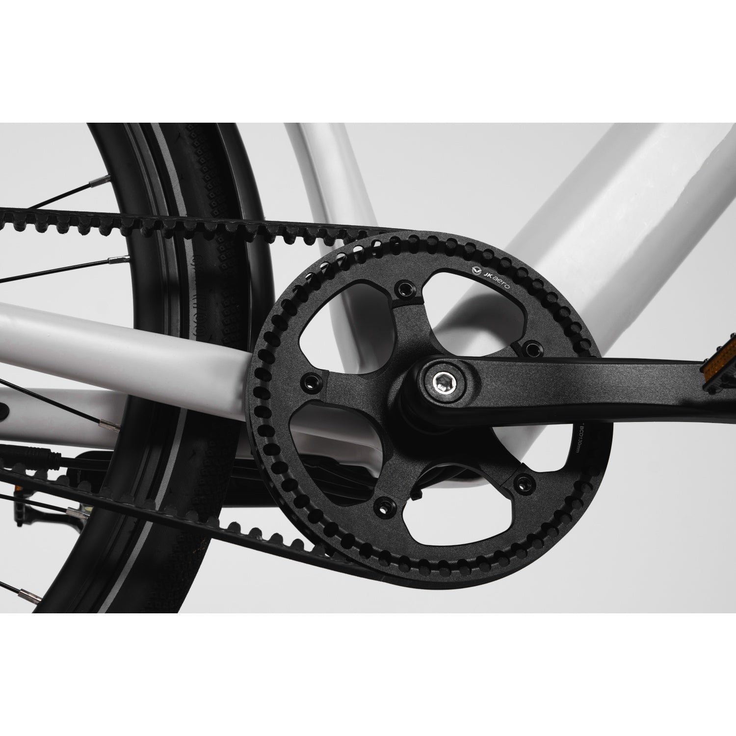 Primer plano de un sistema de transmisión por correa de bicicleta negro con plato dentado y cuadro blanco.
