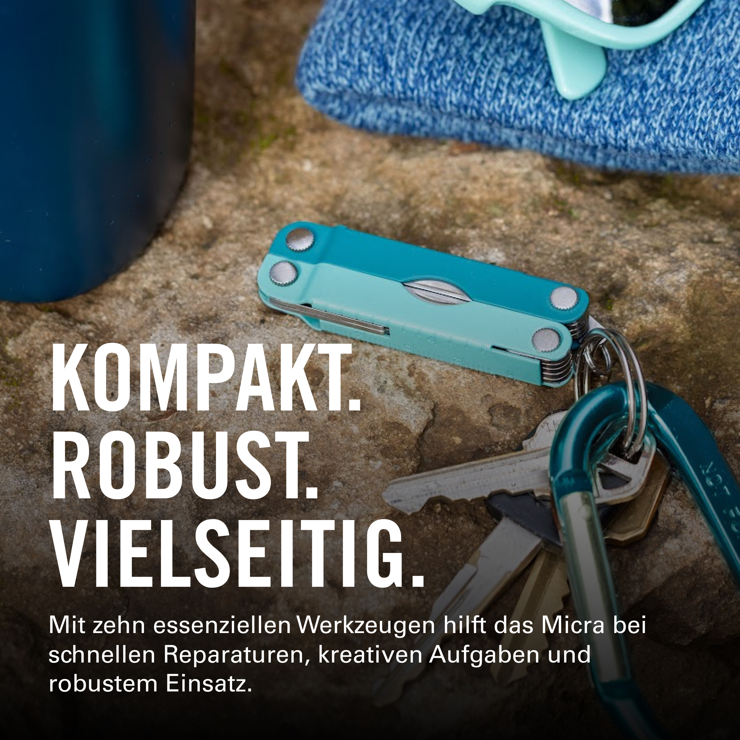 Ein blaues Multitool mit Schlüsseln und einem Karabiner auf Stein.