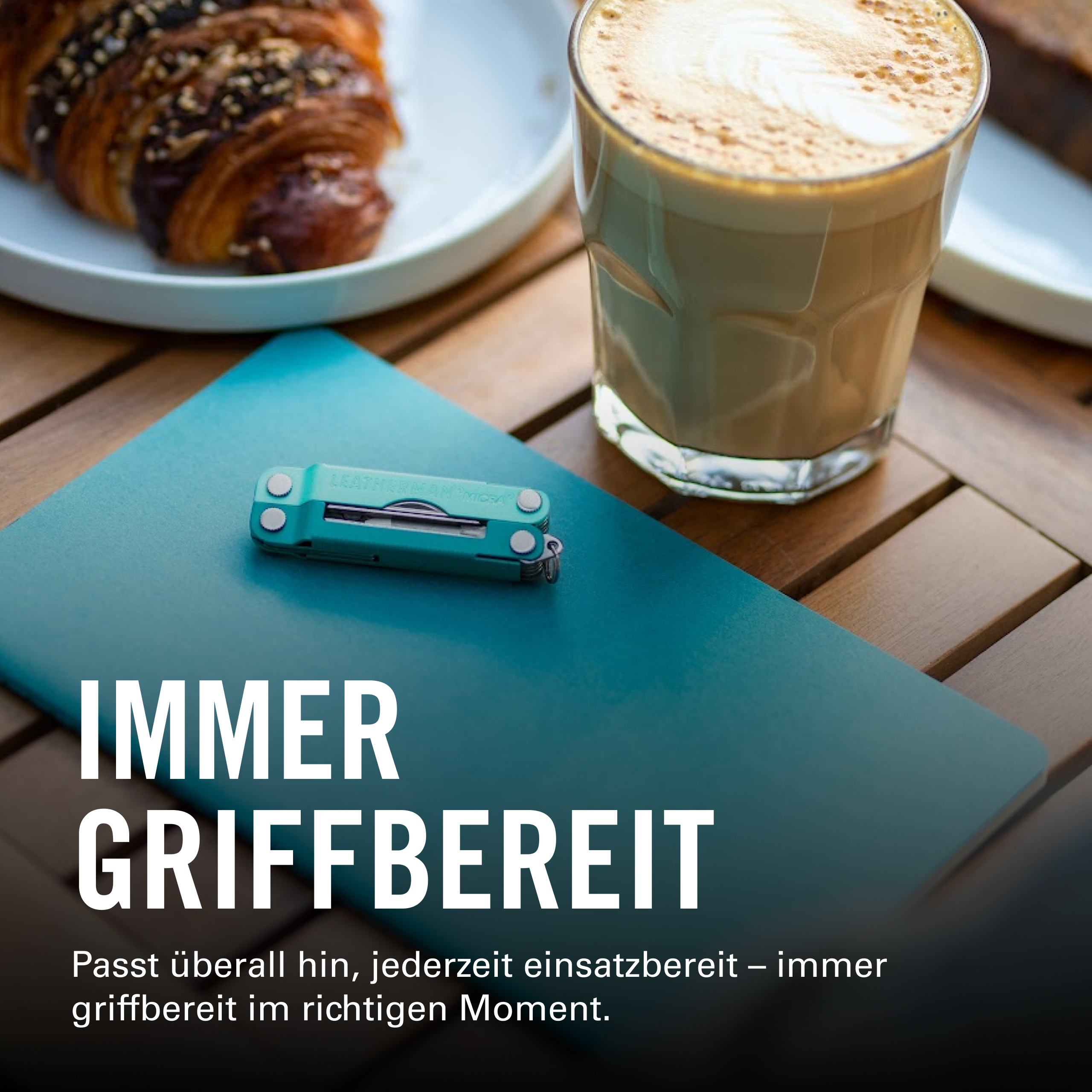 Ein Croissant, Kaffee und ein Multitool auf einem Holztisch.