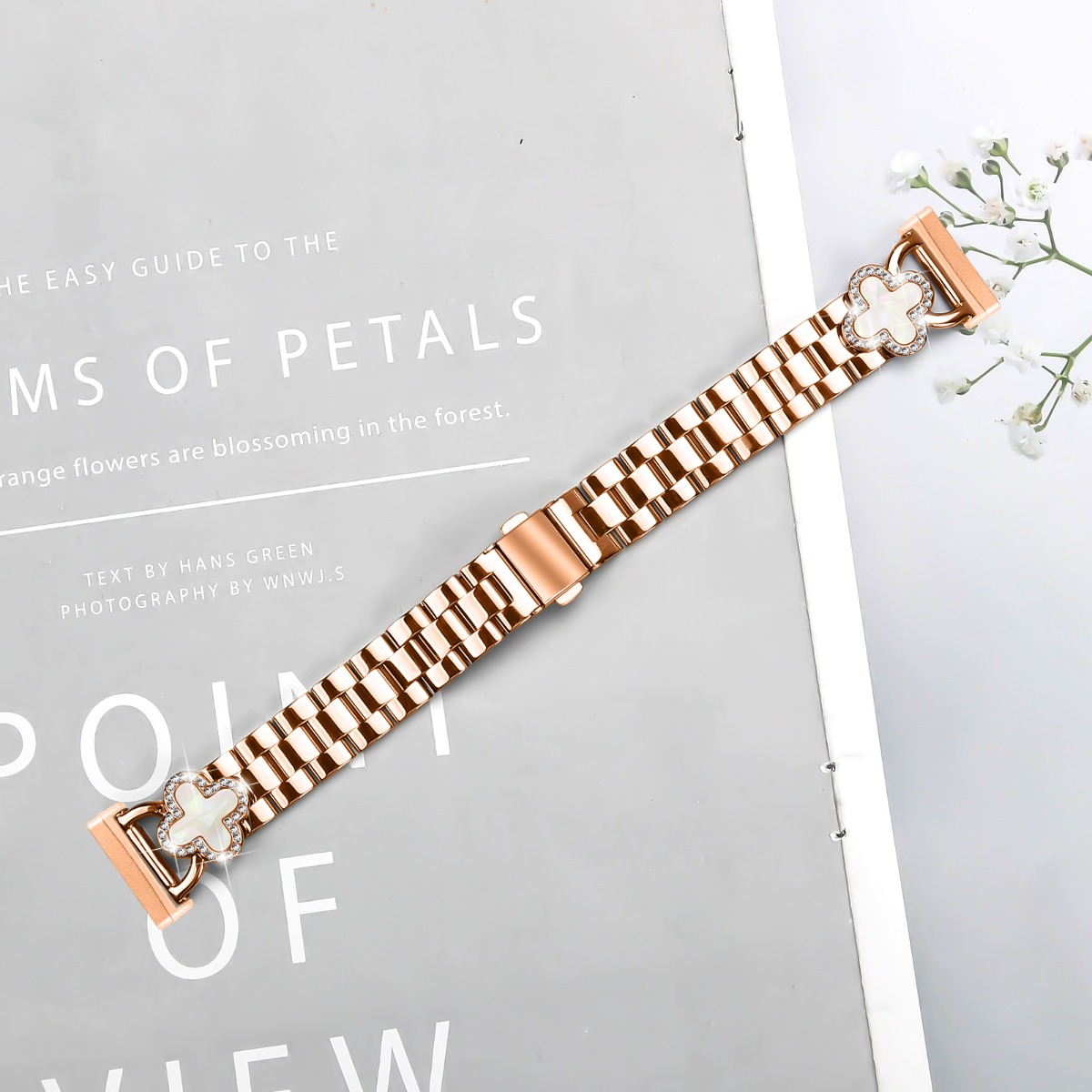 Roségoldenes Uhrenarmband mit Kleeblattanhängern und Diamanten auf einem Buch.