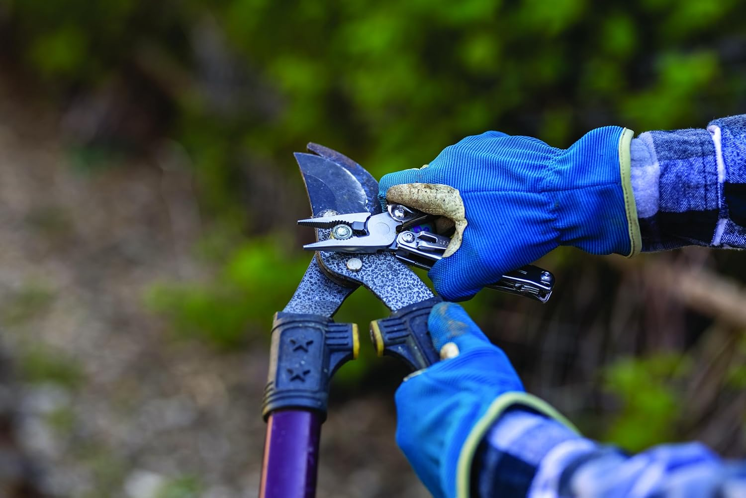 Hände in blauen Handschuhen benutzen eine Gartenschere mit Multitool-Aufsatz.