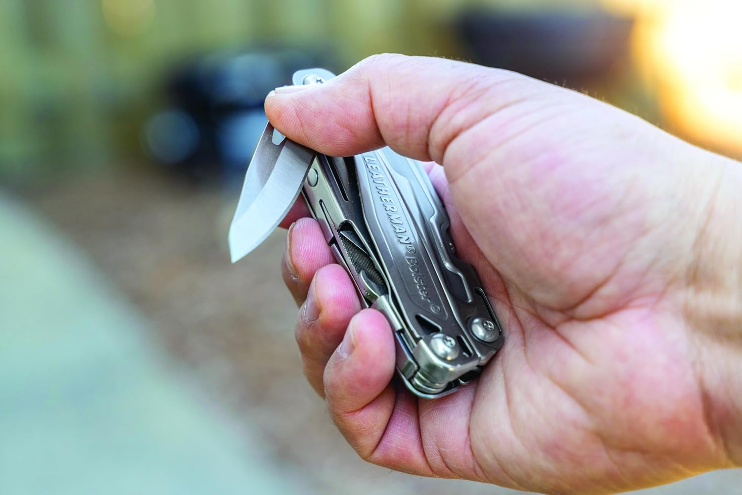 Eine Hand hält ein silbernes Multitool mit ausgeklappter Klinge im Freien.