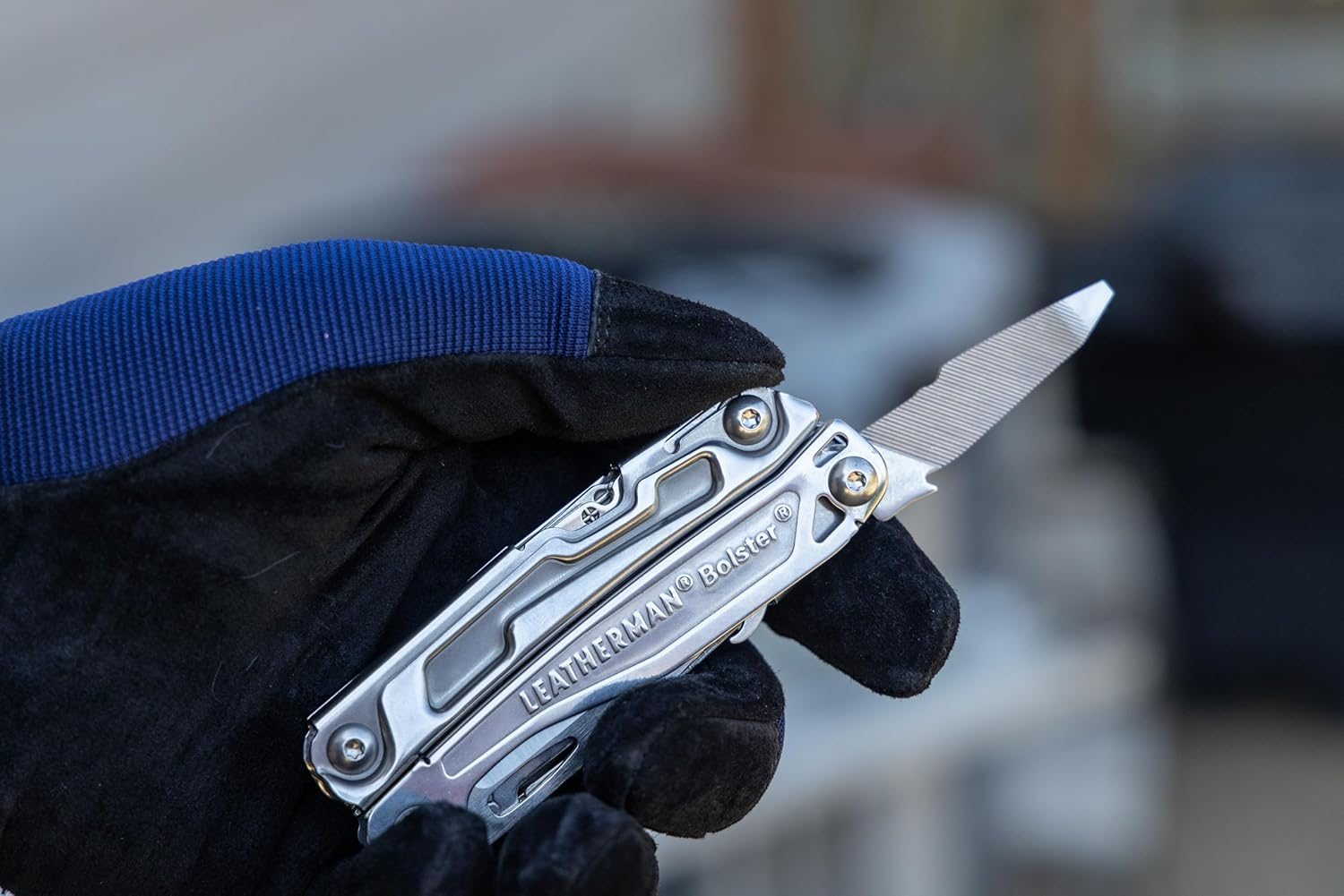 Eine Hand in schwarzem Handschuh hält ein silbernes Multitool mit geöffneter Feile.
