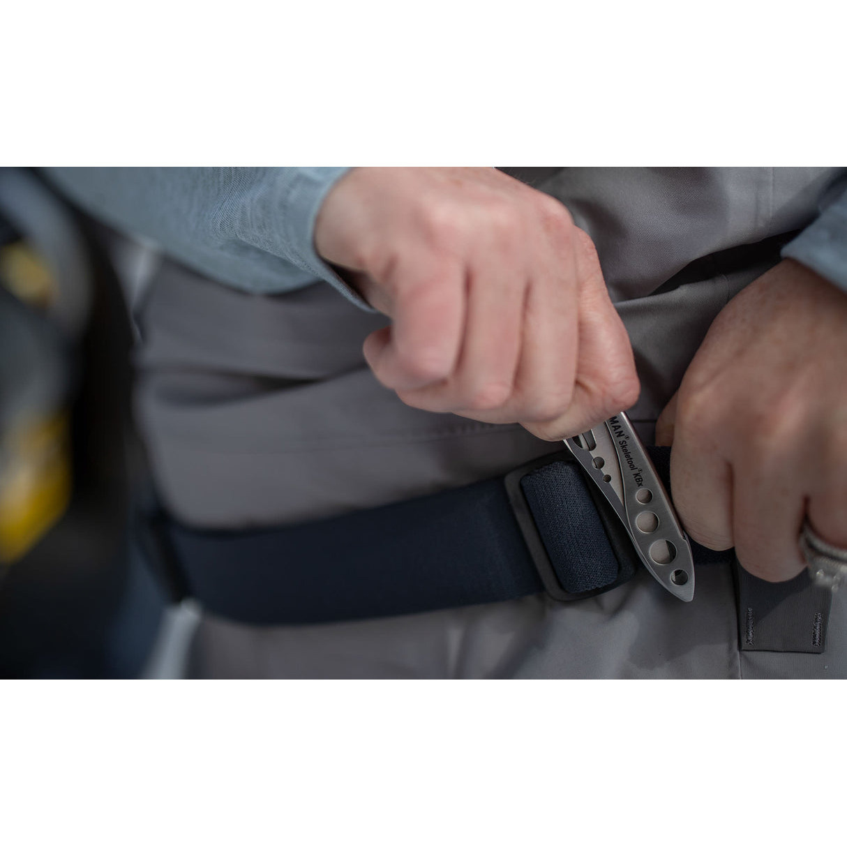 Hände befestigen einen dunkelblauen Gürtel mit einem silbernen Leatherman Multitool.