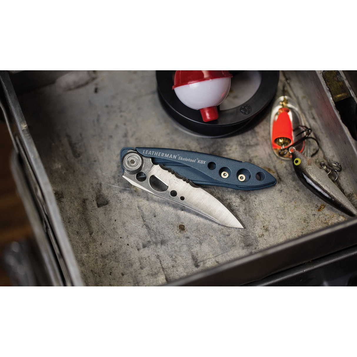 Ein blaues Leatherman Multitool liegt neben Fischködern und einer Angelpose.