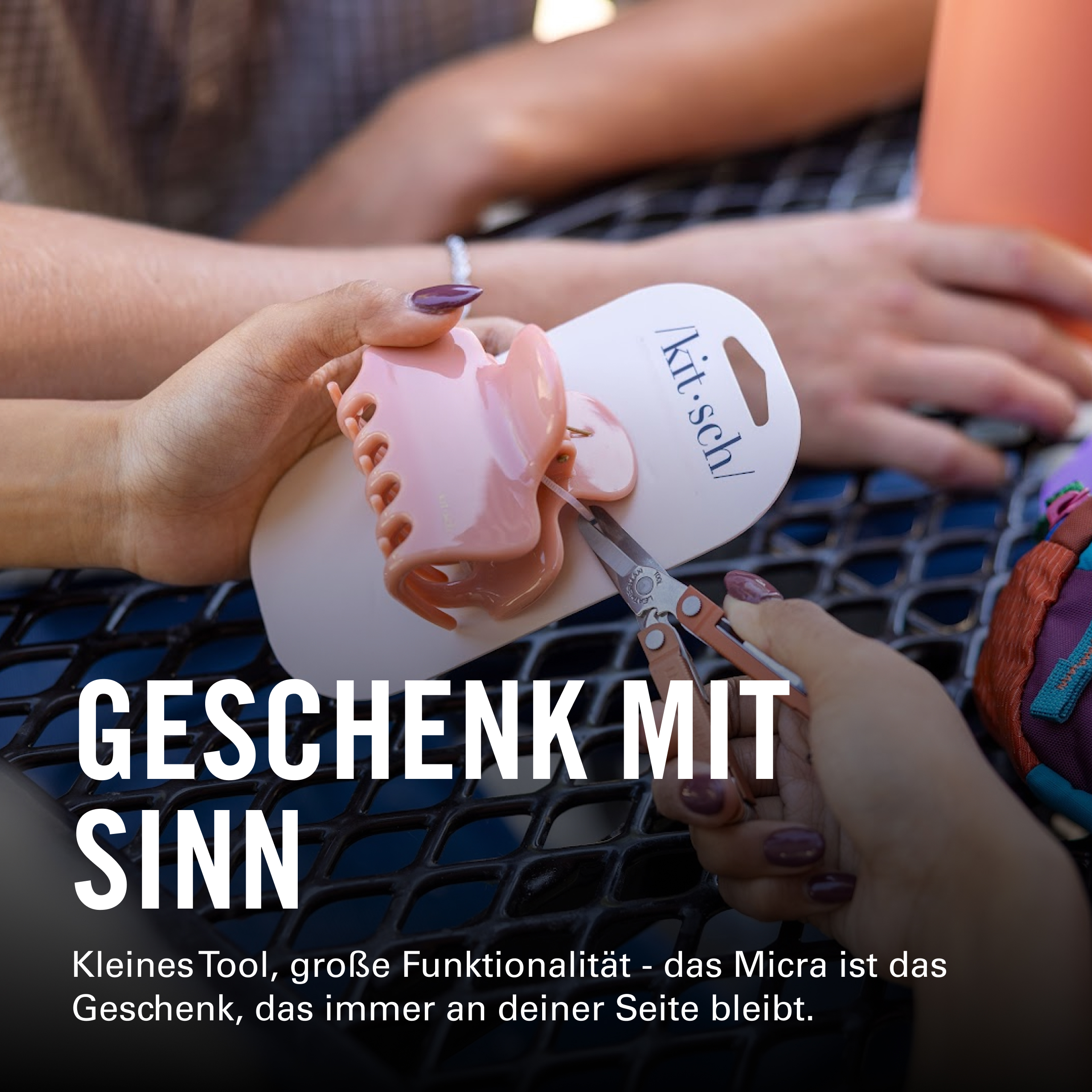 Hände halten eine rosa Haarklammer und eine kleine Schere.